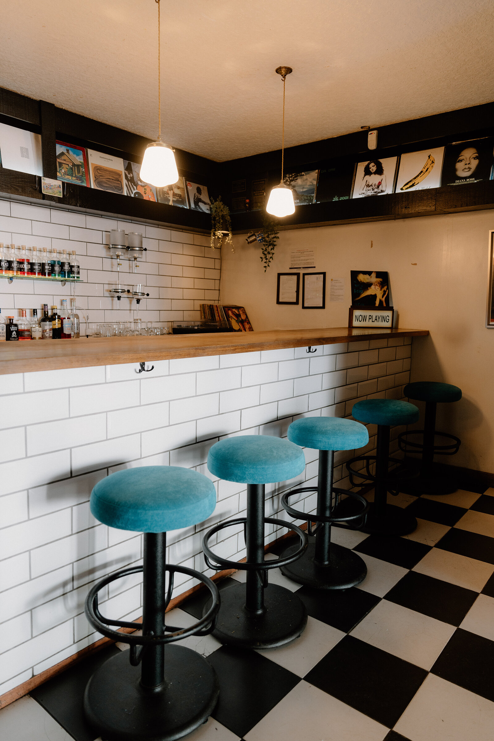A Now Playing sign sits on a subway-tiled bar counter beneath shelves of vinyl records in Edinburgh.