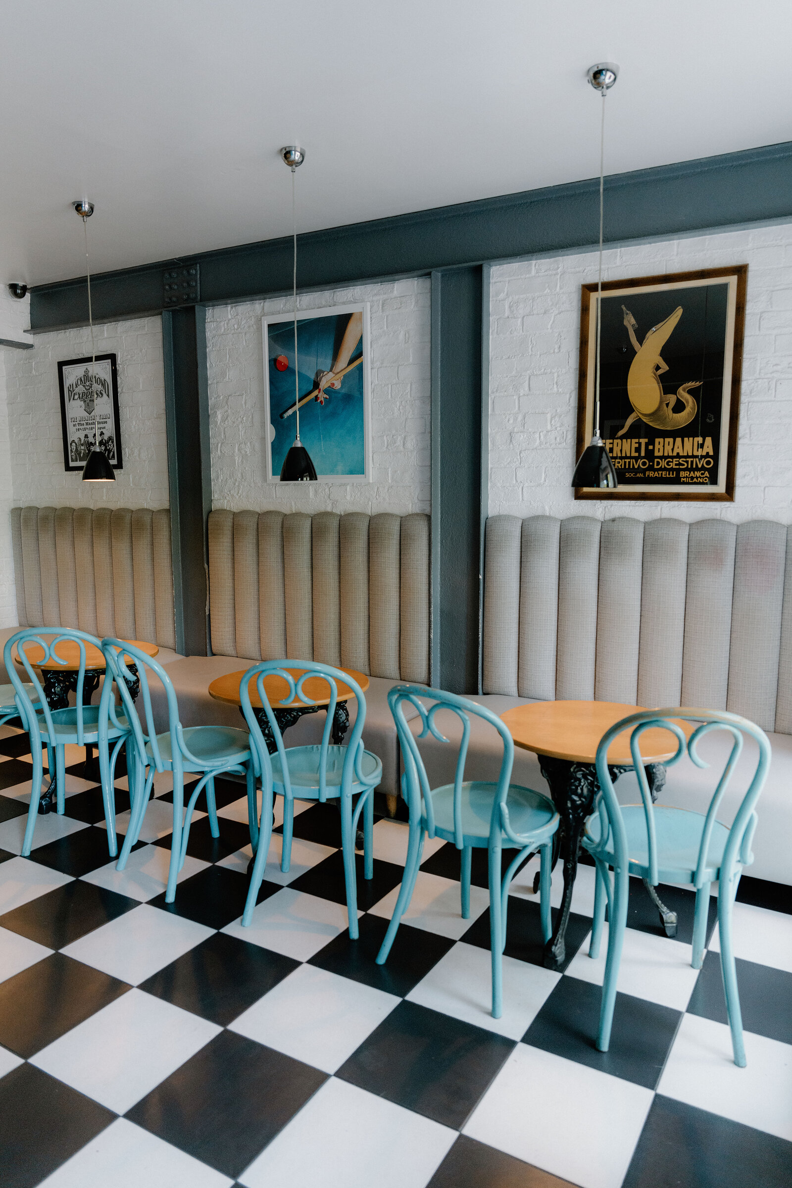 Teal bentwood chairs surround wooden tables beneath vintage posters on a checkerboard floor in an Edinburgh bar.
