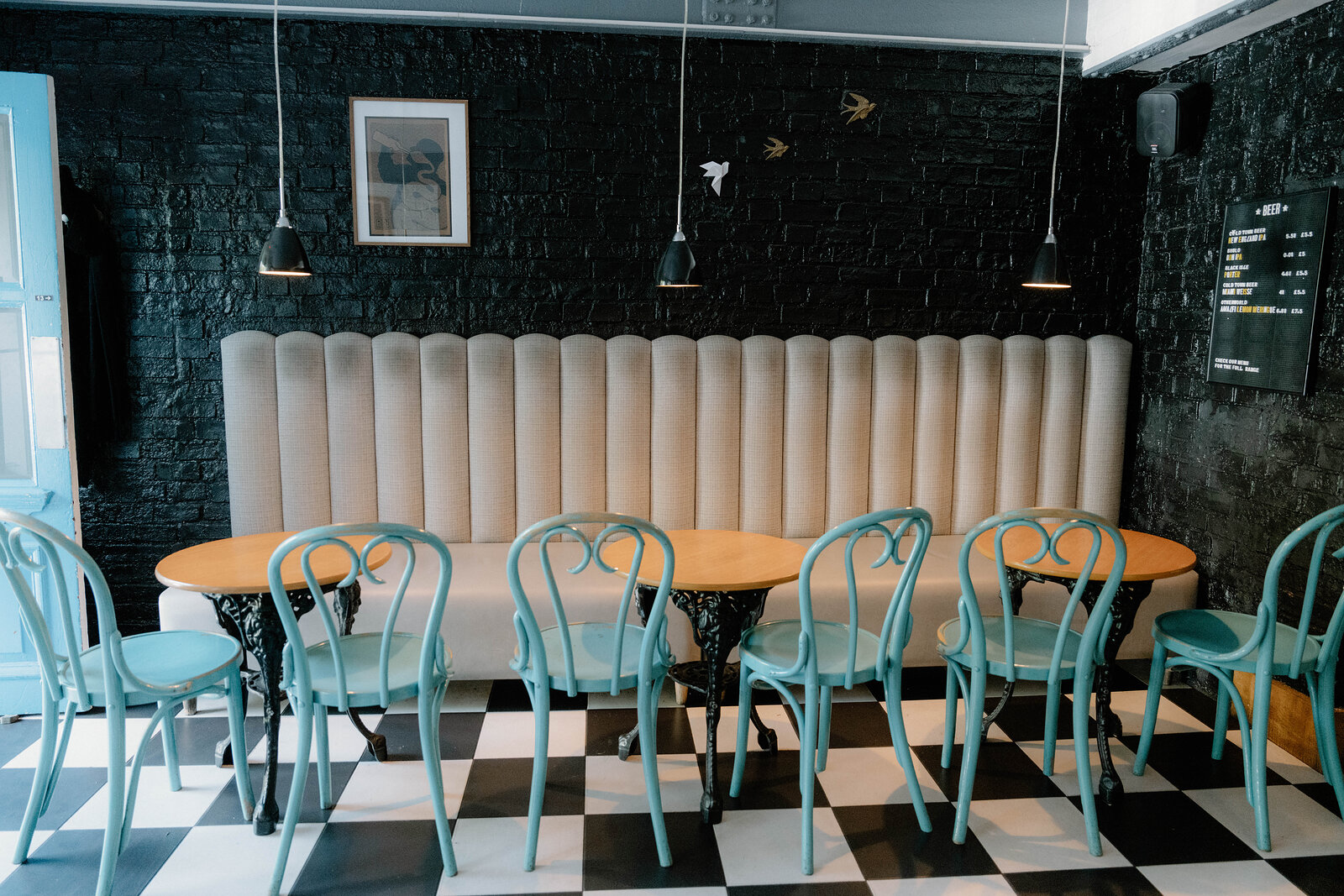 A beige banquette and teal bentwood chairs sit against a black brick wall in an Edinburgh bar.