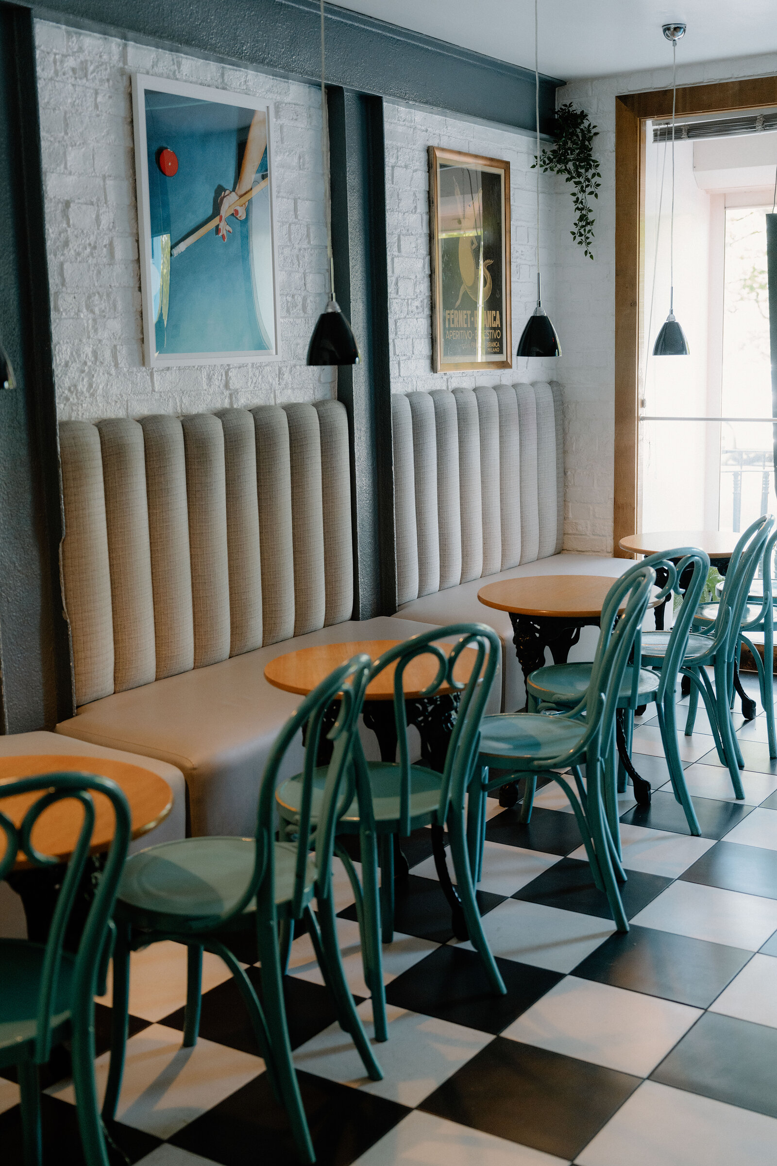 Vintage posters and a trailing plant decorate a seating area with teal bentwood chairs at The Lucky Liquor Co, Edinburgh.