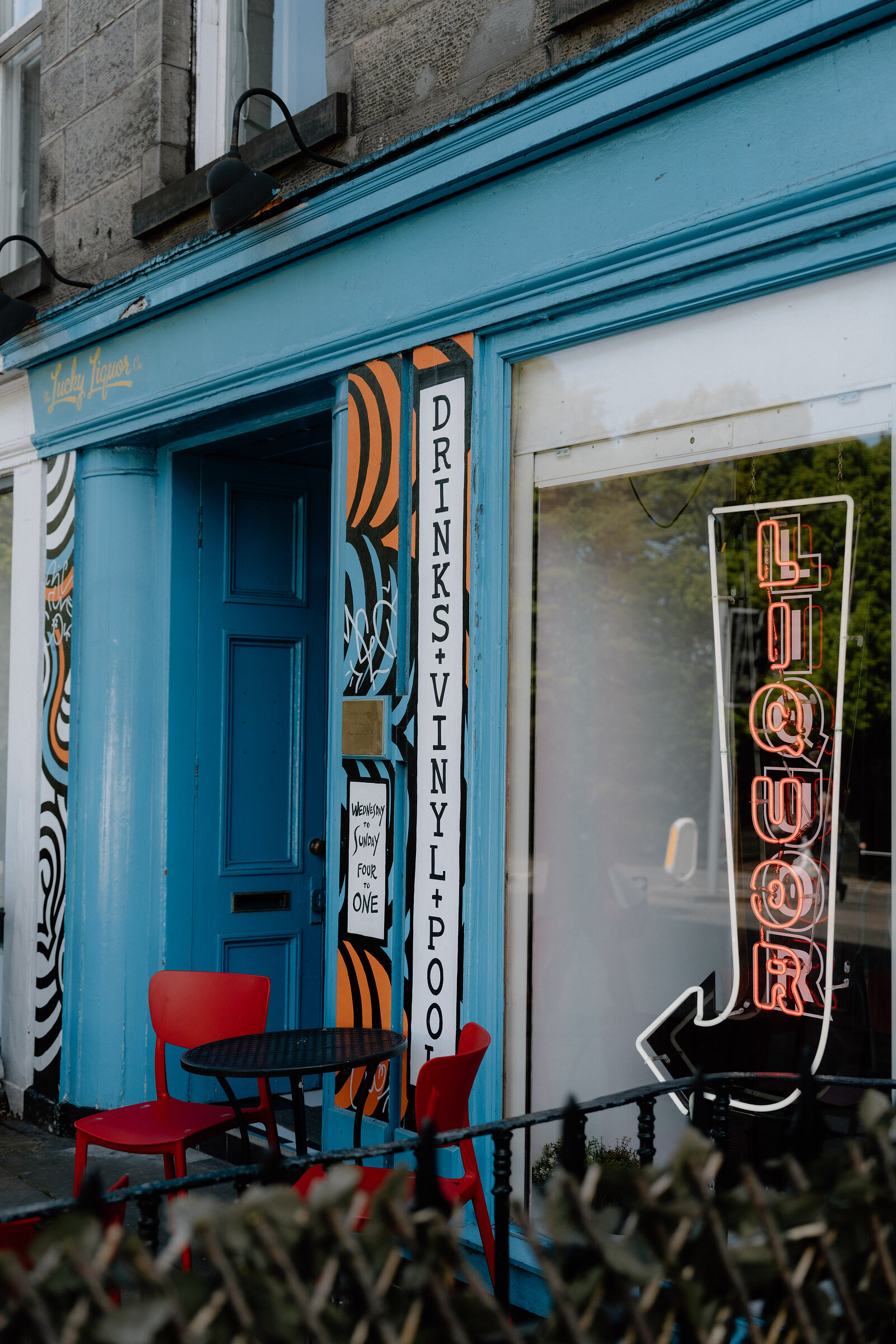 A neon Liquor sign and Drinks, Vinyl and Pool lettering mark The Lucky Liquor Co's blue doorway in Edinburgh.