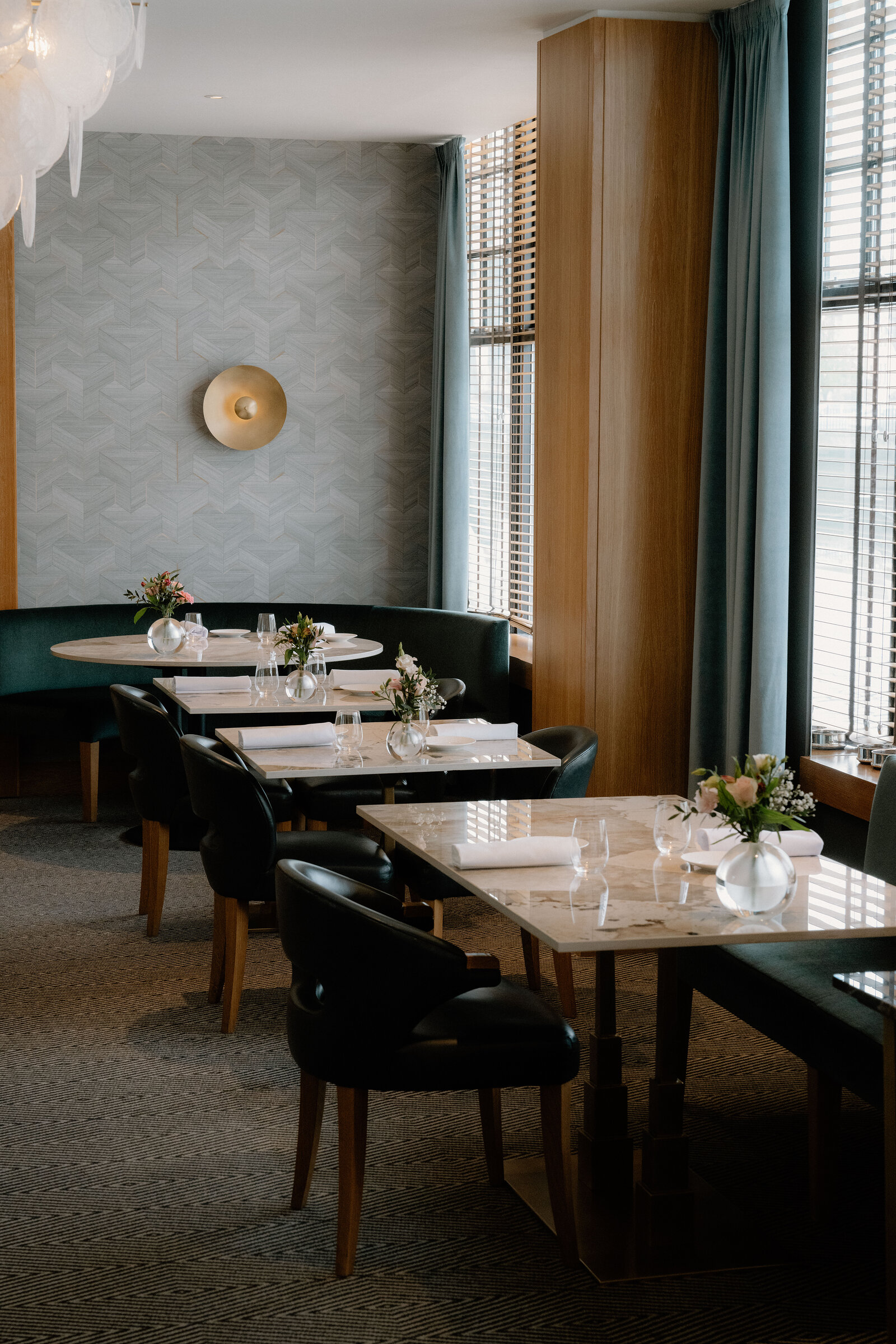Black leather chairs surround marble-topped tables beneath teal curtains in an Edinburgh restaurant.