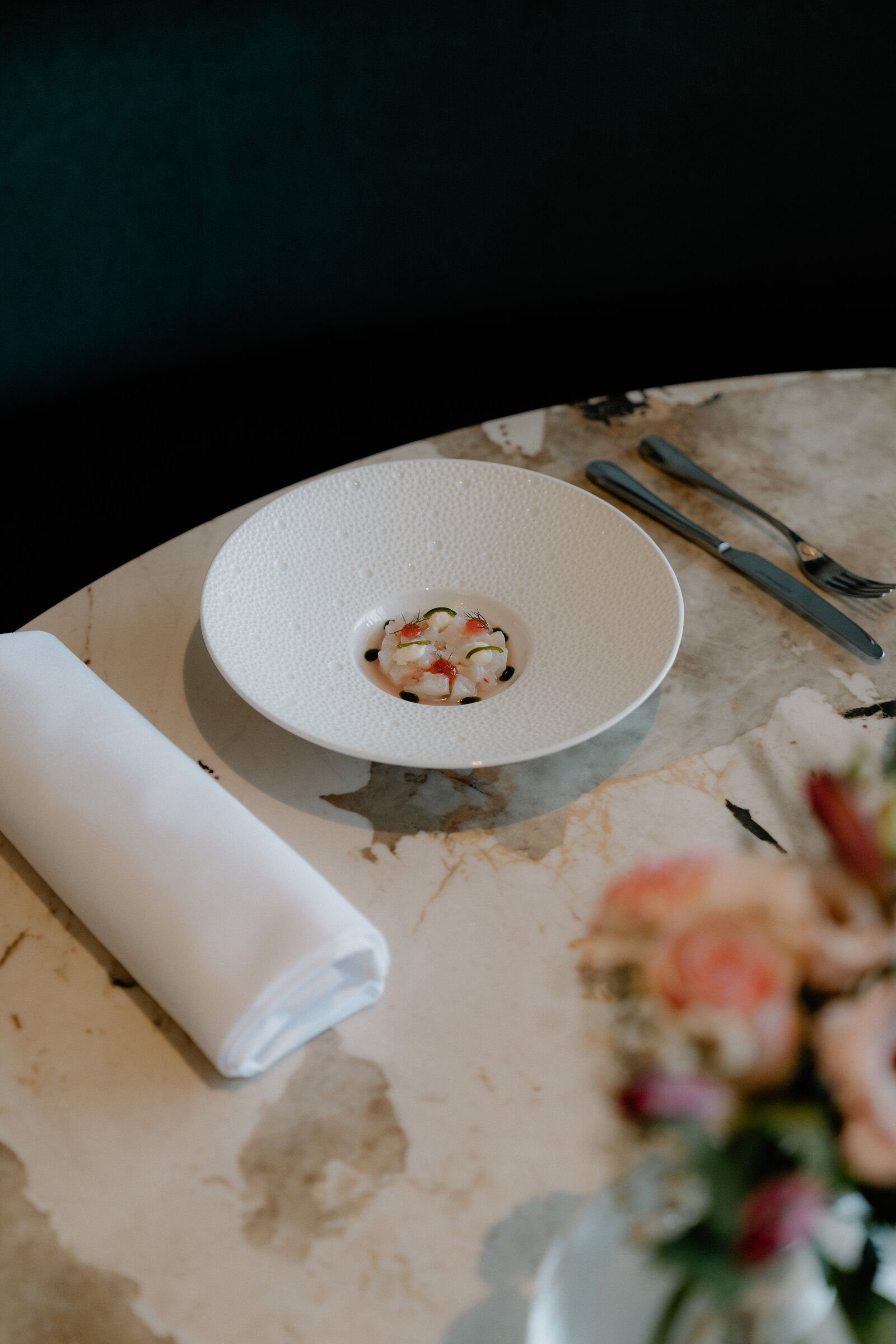 A rolled napkin and seafood starter sit on a marble table beside a vase of flowers in an Edinburgh restaurant.