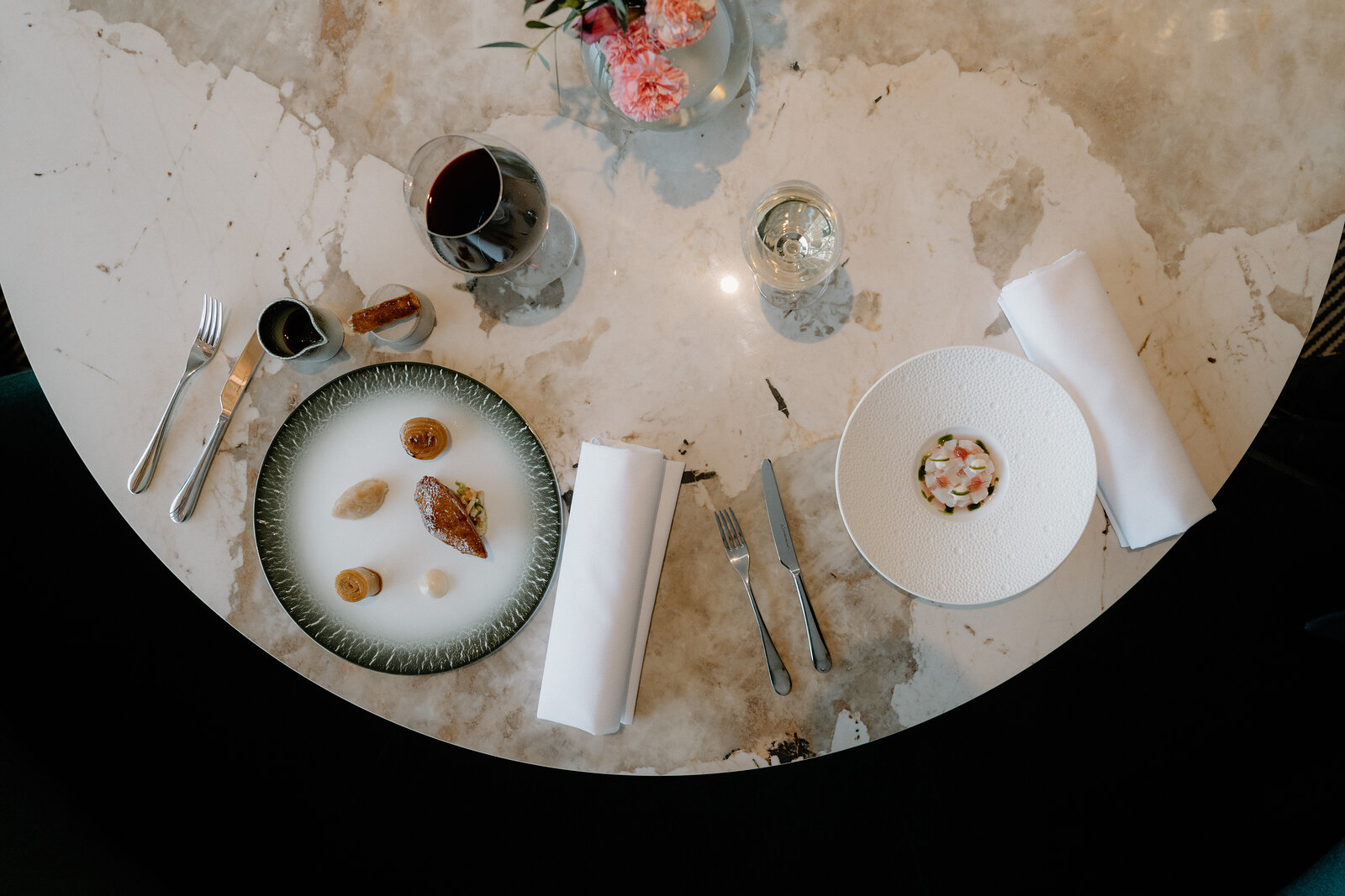 Two plated courses sit beside glasses of wine and a small vase of flowers on a marble table in an Edinburgh restaurant.