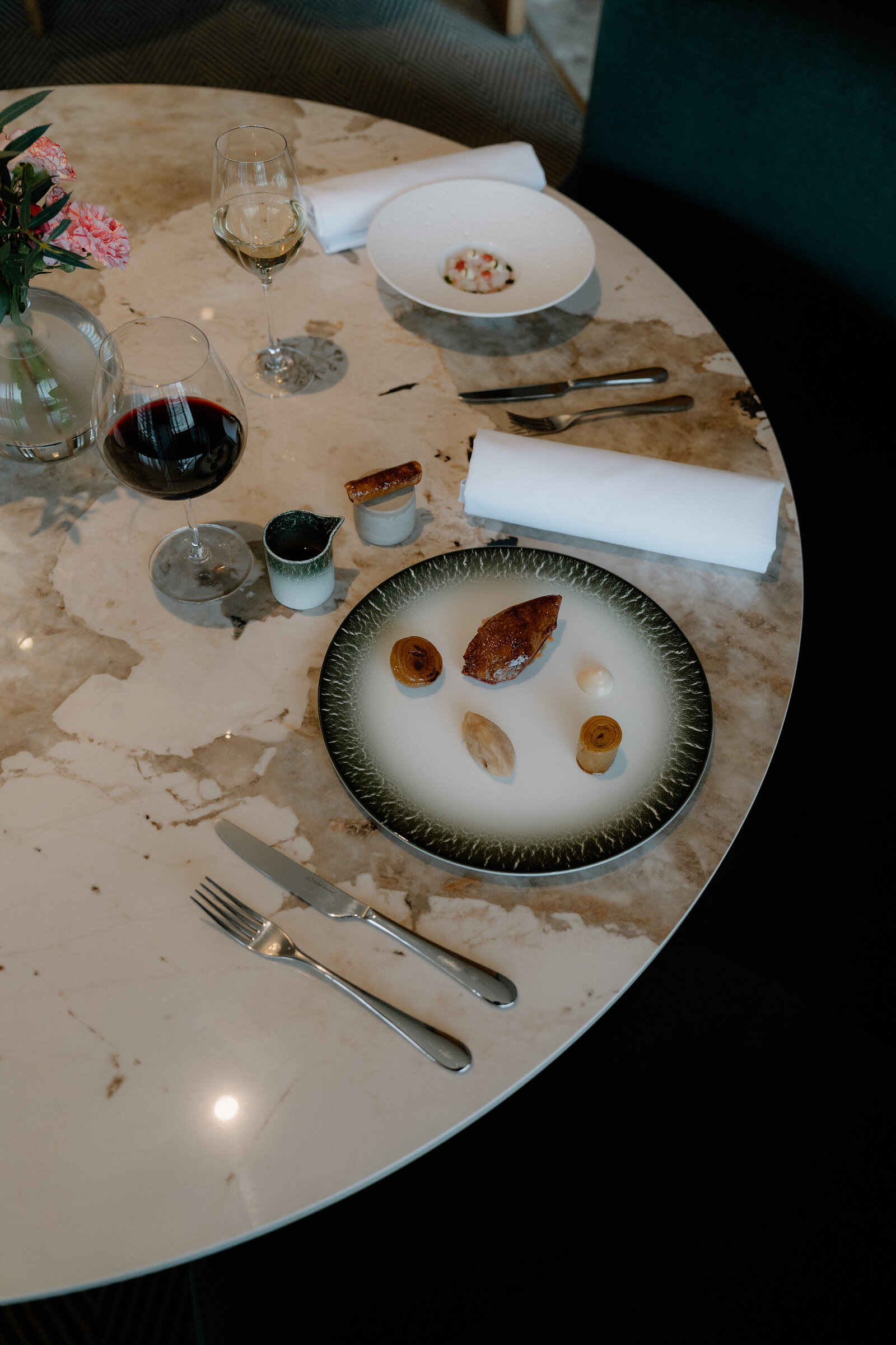A plated dish, wine glasses and pink flowers are arranged on a marble table in an Edinburgh restaurant.