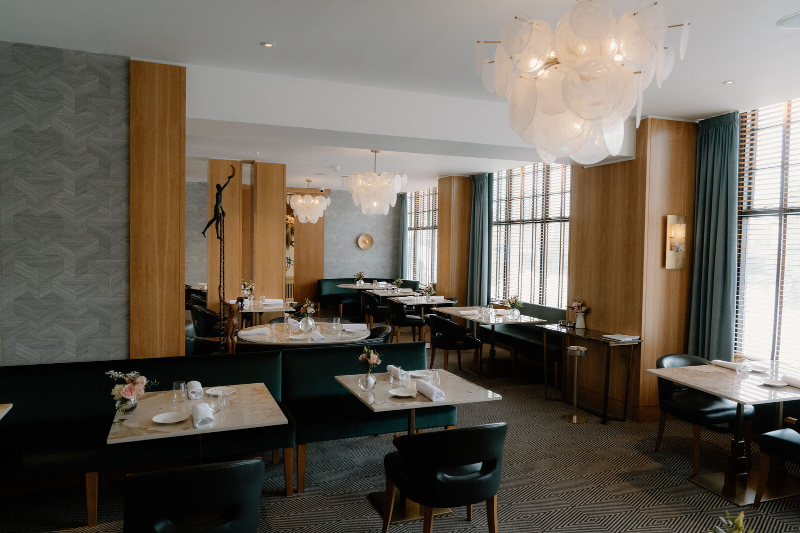 Green velvet banquettes and marble tables sit beneath cluster pendant lights in an Edinburgh restaurant.