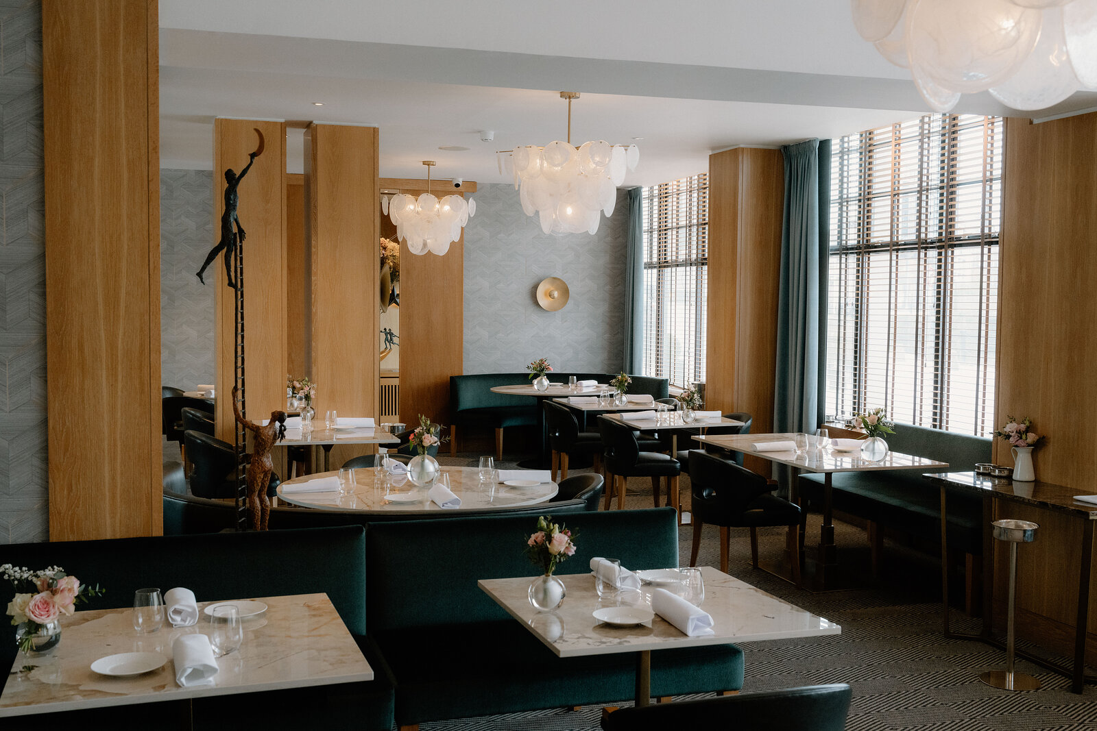 Cluster pendant lights hang above green banquette seating and marble tables in an Edinburgh restaurant.