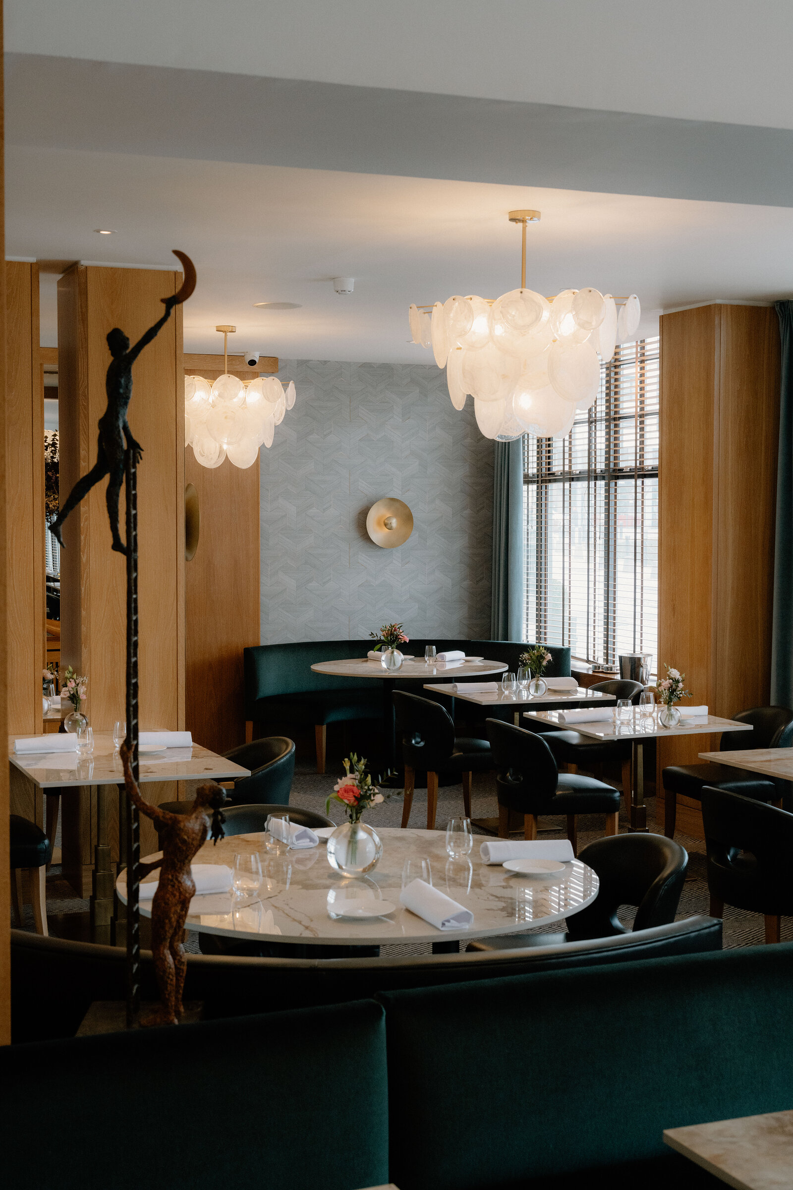 Bronze figures perch on plinths beneath cluster glass chandeliers in the dining room at Restaurant Martin Wishart, Edinburgh.