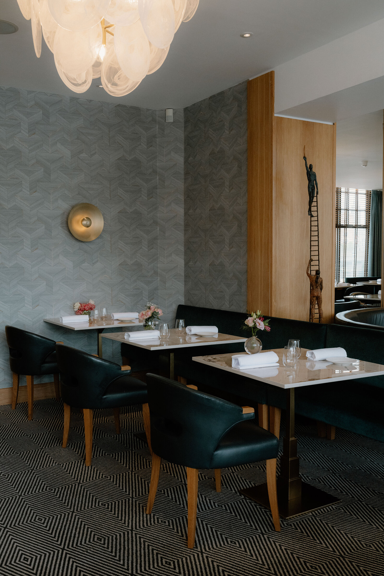 Green velvet banquettes curve beneath a chandelier and patterned wallpaper at Restaurant Martin Wishart, Edinburgh.
