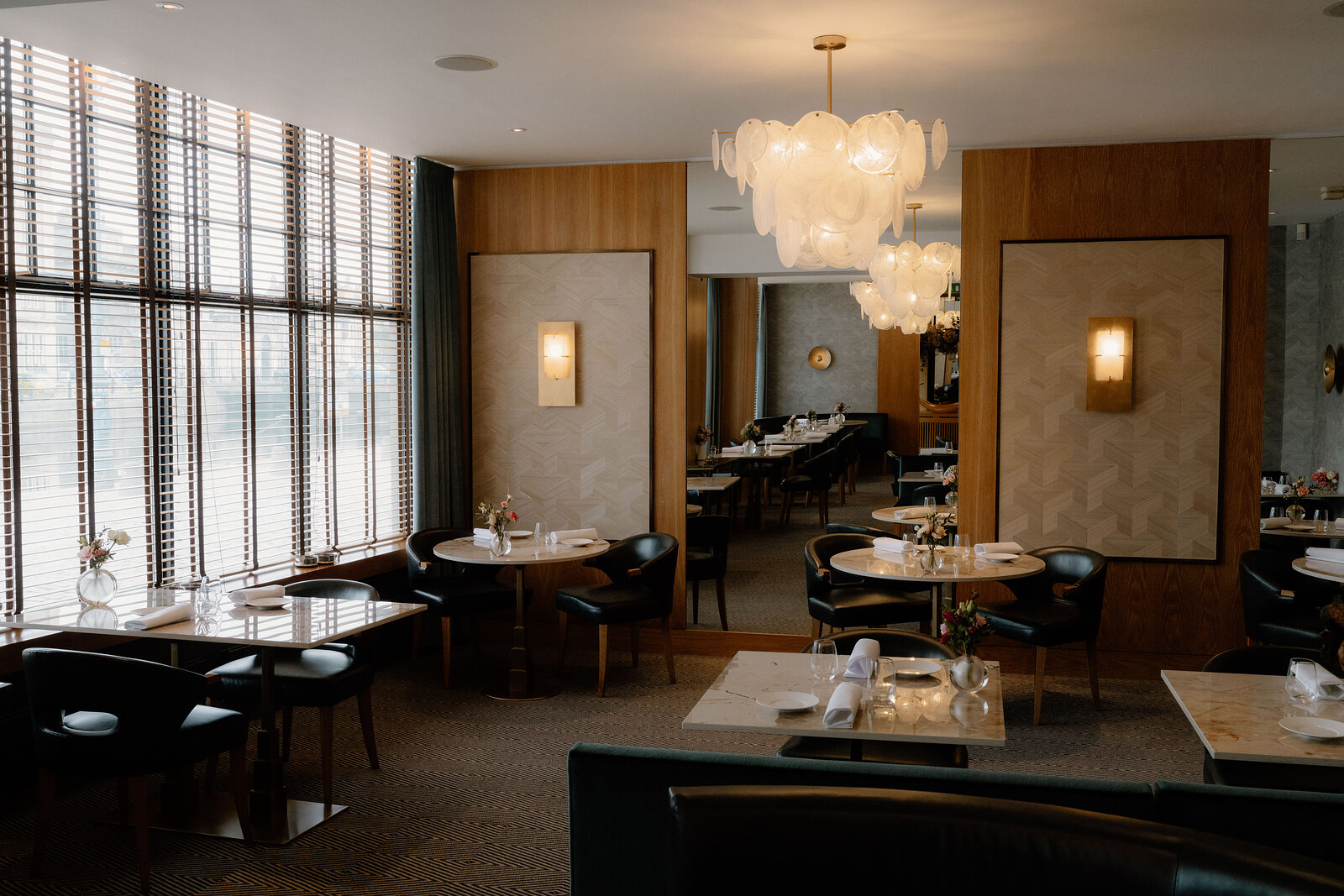 Cluster chandeliers hang above marble tables and dark timber panelling at Restaurant Martin Wishart, Edinburgh.