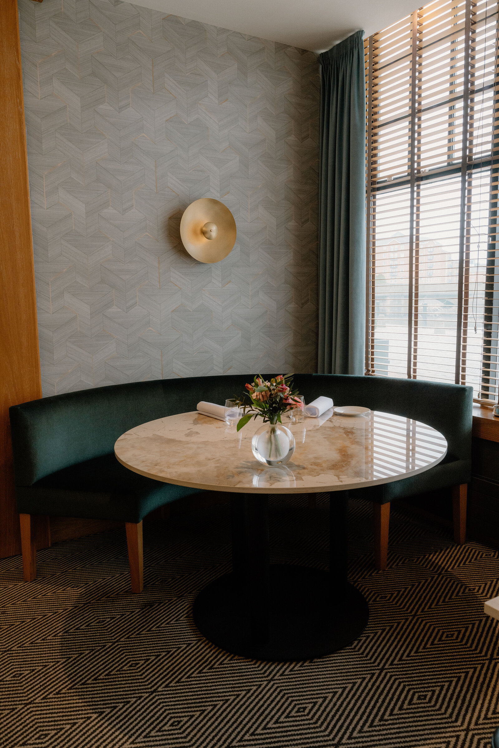 A curved green banquette and marble table sit beneath a brass wall light at Restaurant Martin Wishart, Edinburgh.