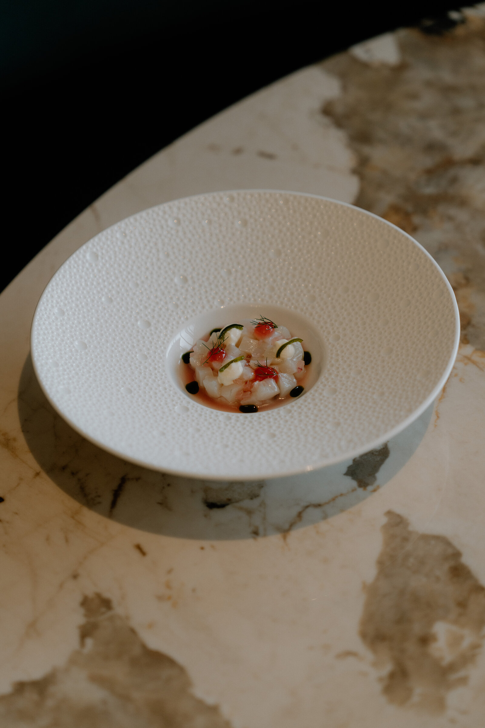 A single seafood course sits at the centre of a wide textured bowl on a marble table at Restaurant Martin Wishart, Edinburgh.