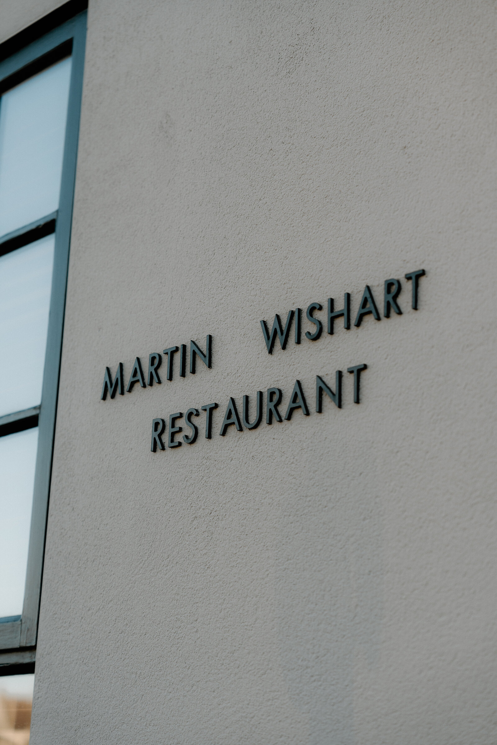 A sign reading Martin Wishart Restaurant is mounted on a white wall in Edinburgh.
