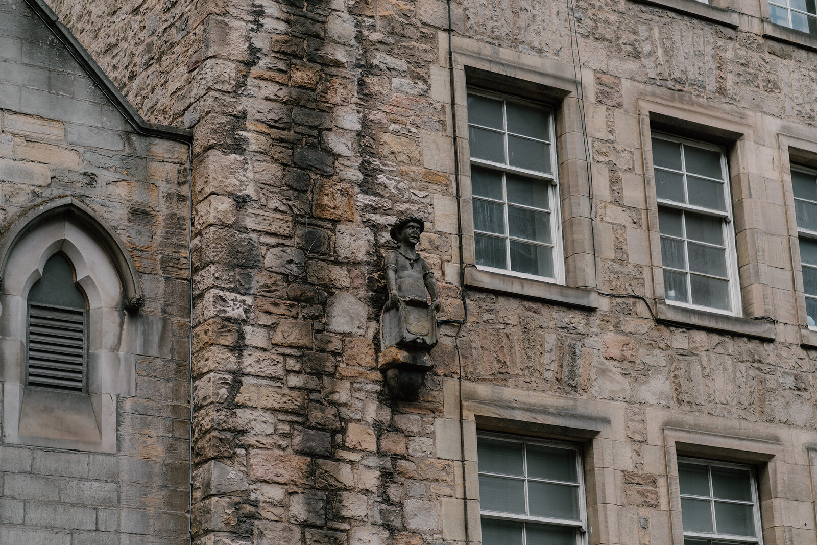 A small carved stone figure is set into the corner of a sandstone building in Edinburgh.