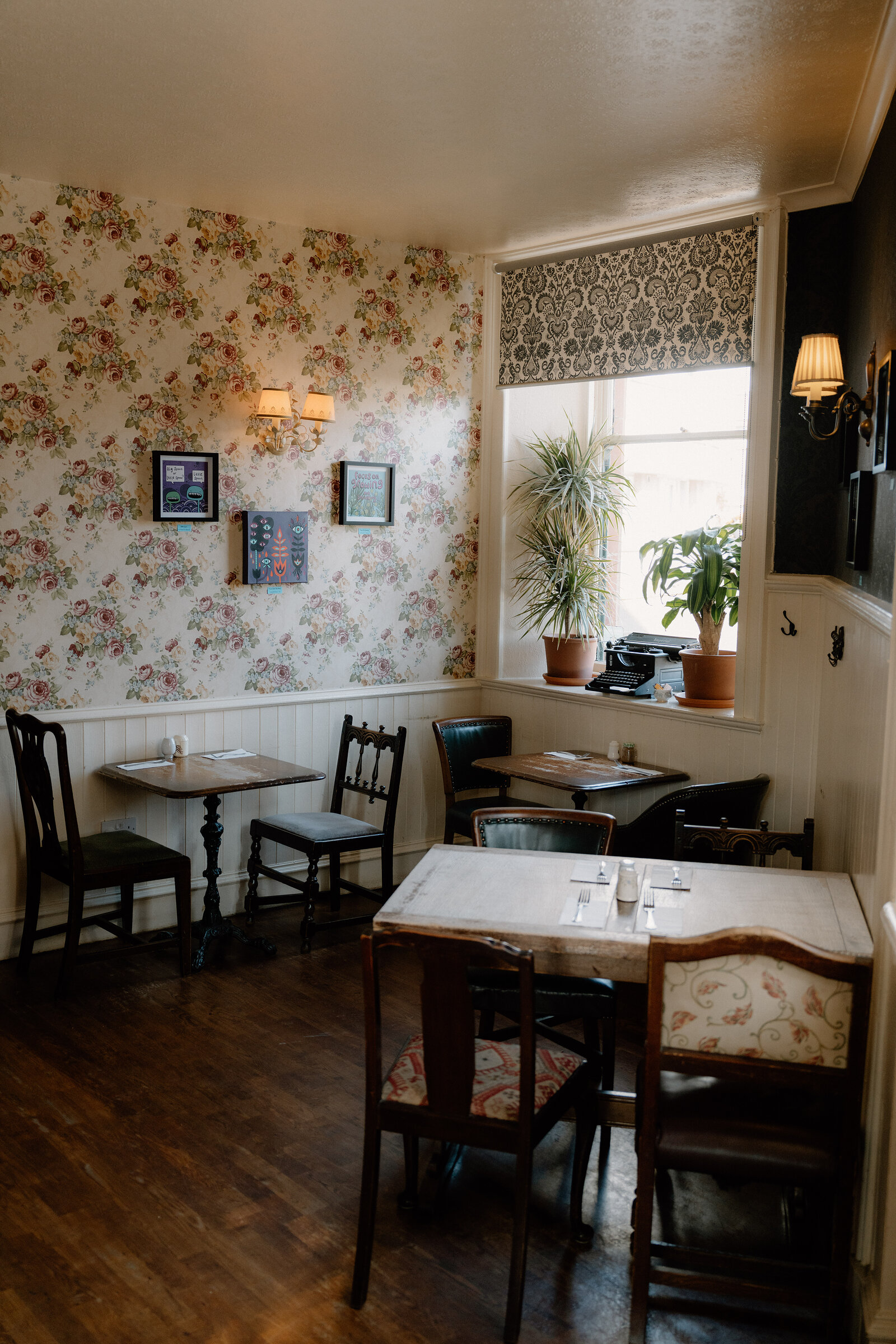 Floral wallpaper and a patterned roman blind line a traditional dining room, potted plants set in the window.