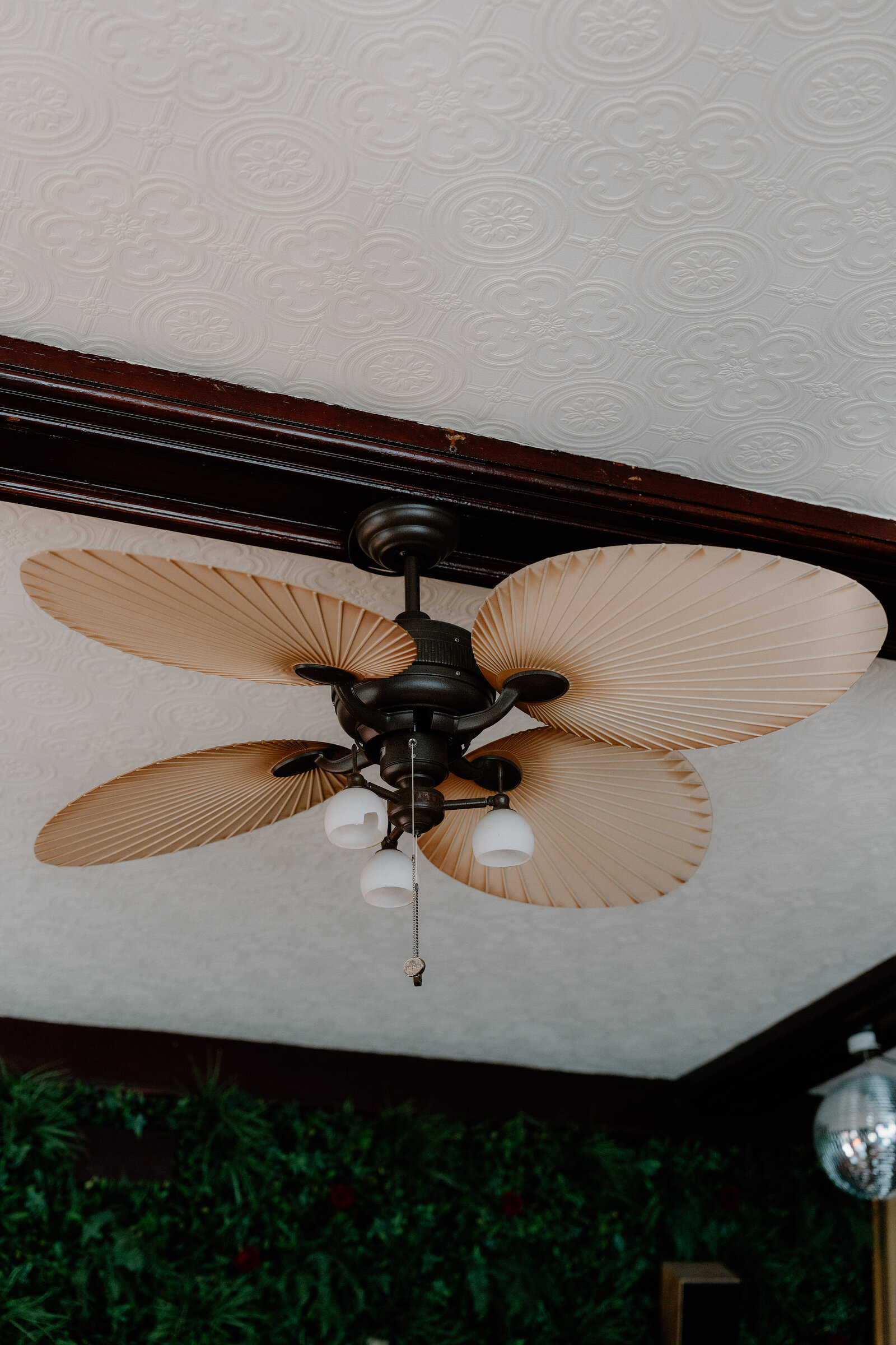 A palm-leaf ceiling fan hangs from a pressed-tin ceiling above dark wood trim.