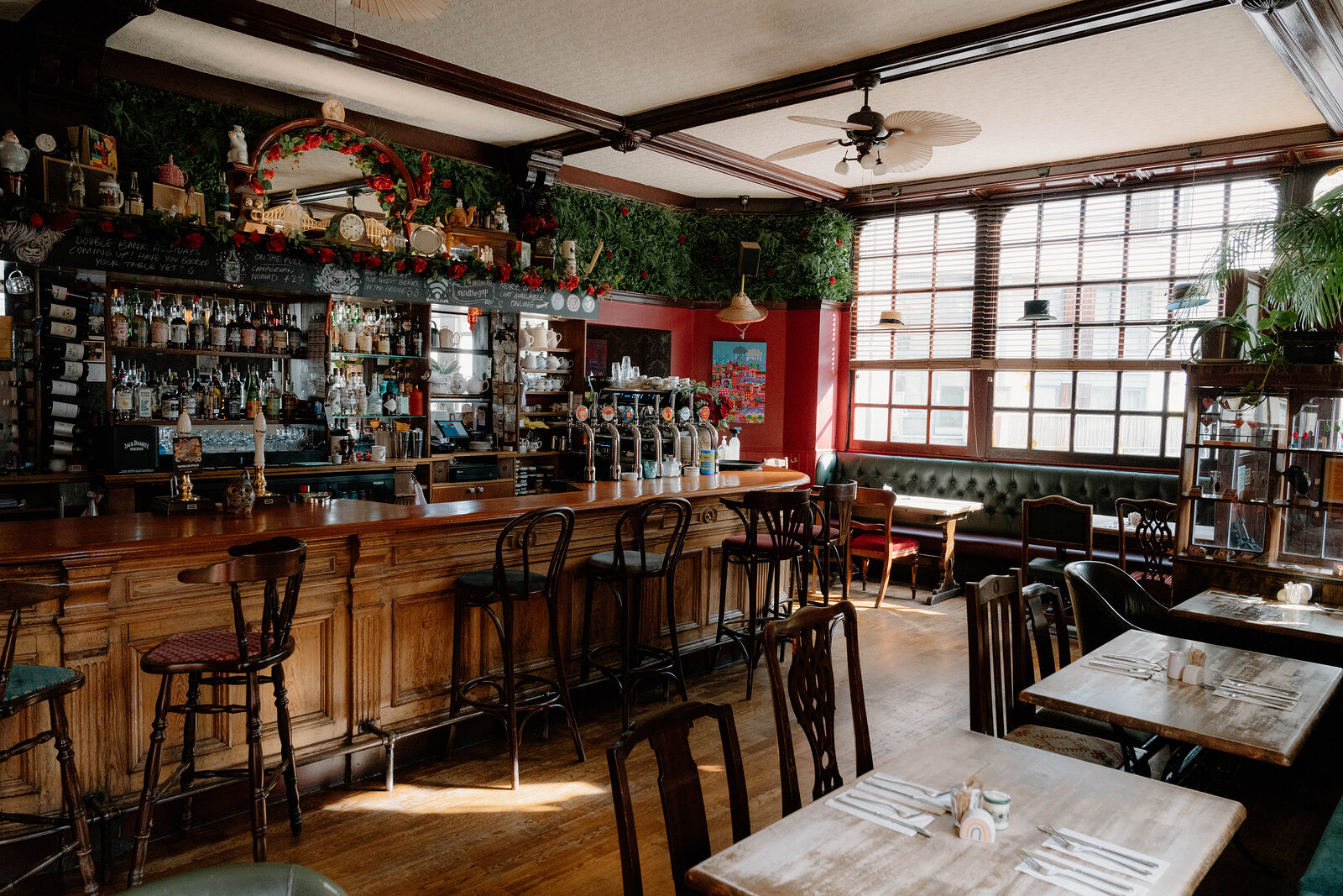 Bottles line a foliage-trimmed bar beside dining tables set against red walls in a pub.