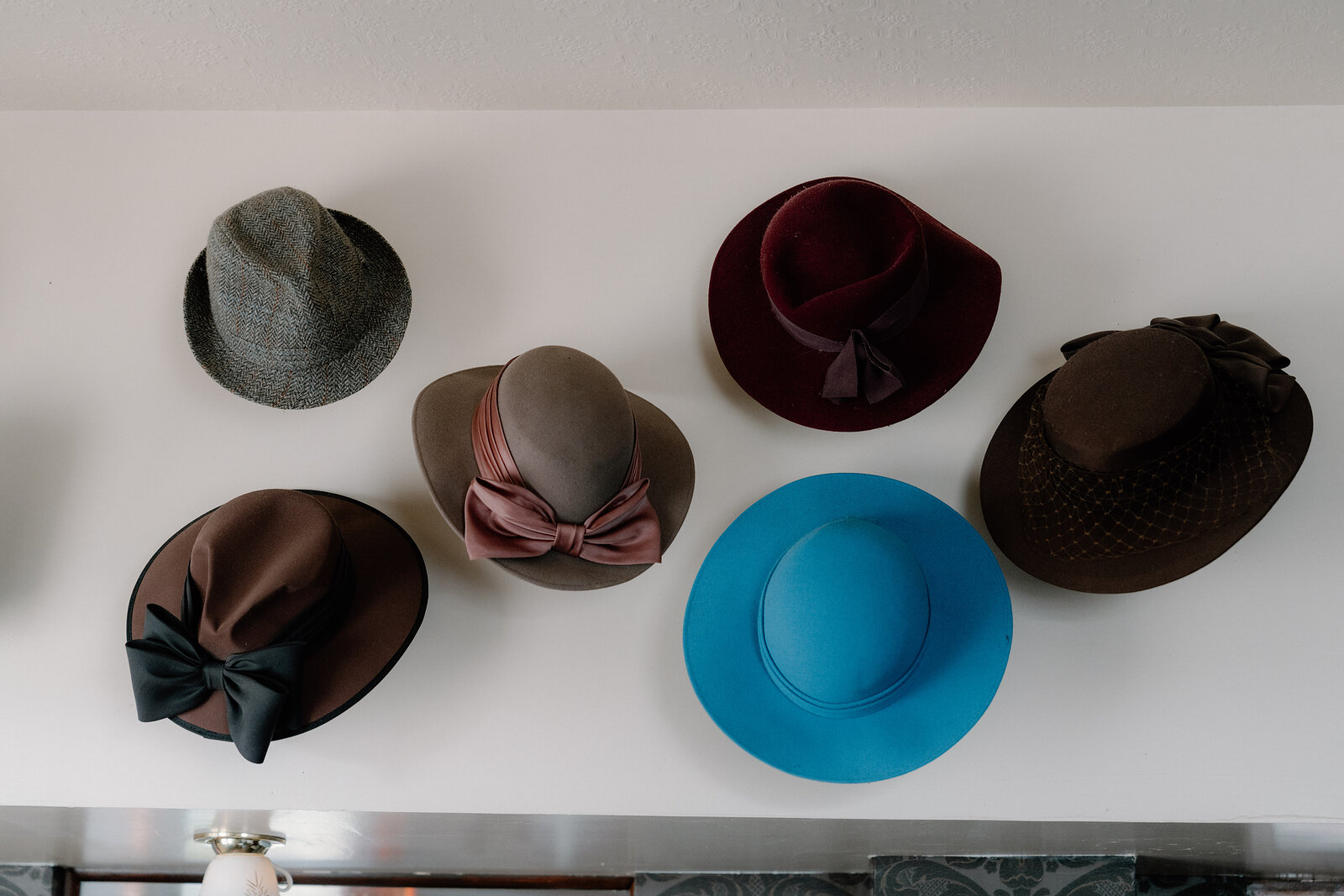 Felt hats in grey, brown, burgundy and blue hang in a row on a white wall.