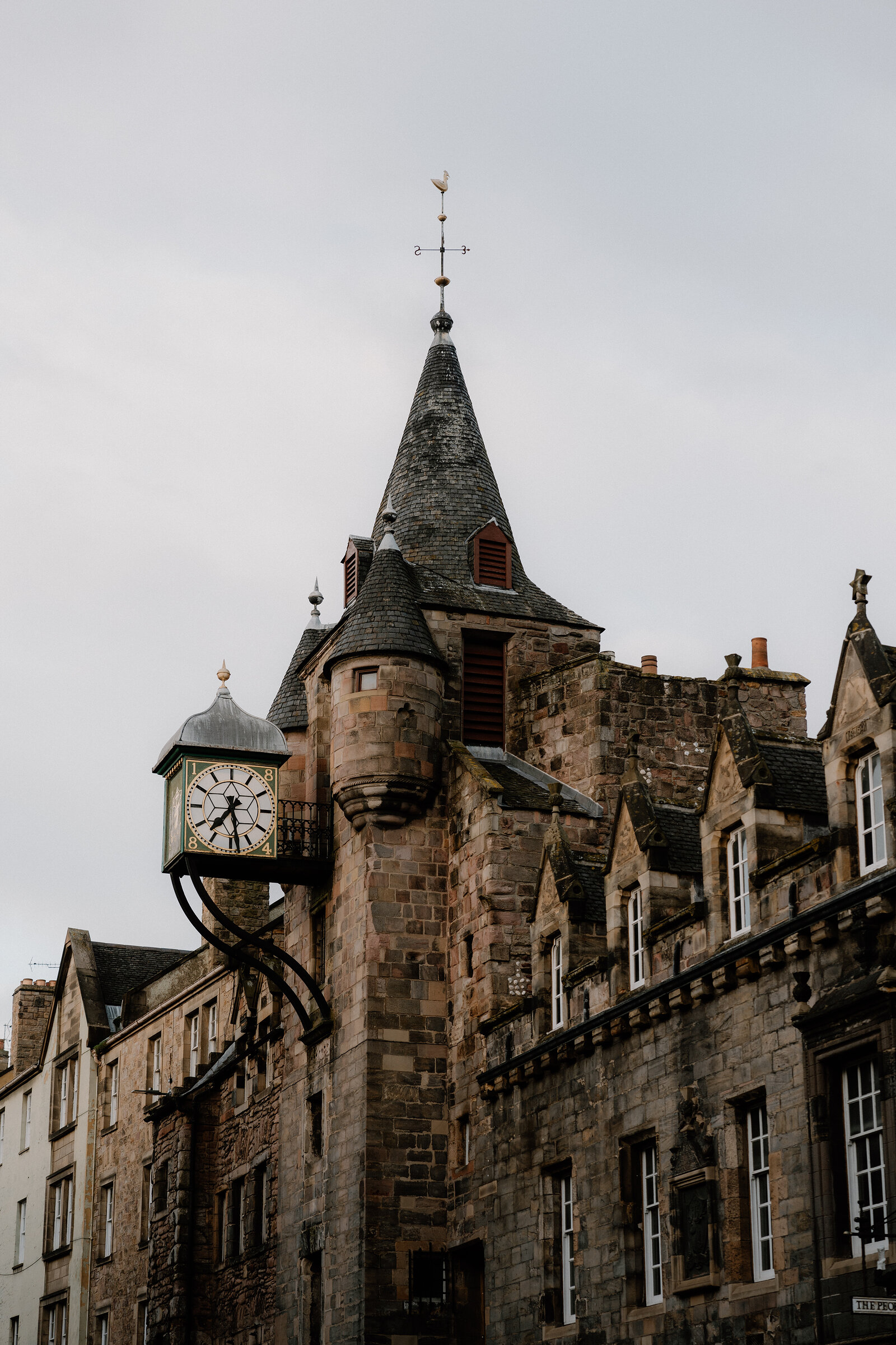A weathervane and clock tower rise above sandstone tenements on the Royal Mile.