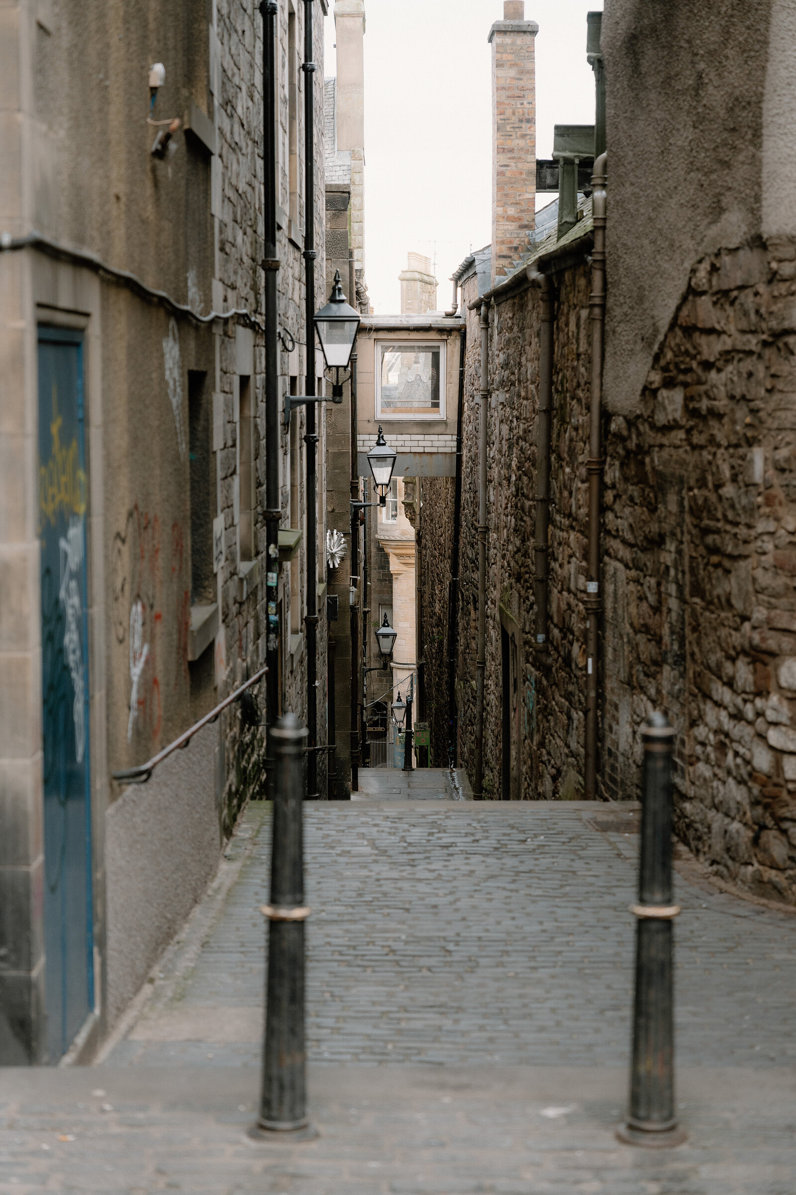 Lampposts line a narrow cobbled close descending between stone tenement walls on the Royal Mile.