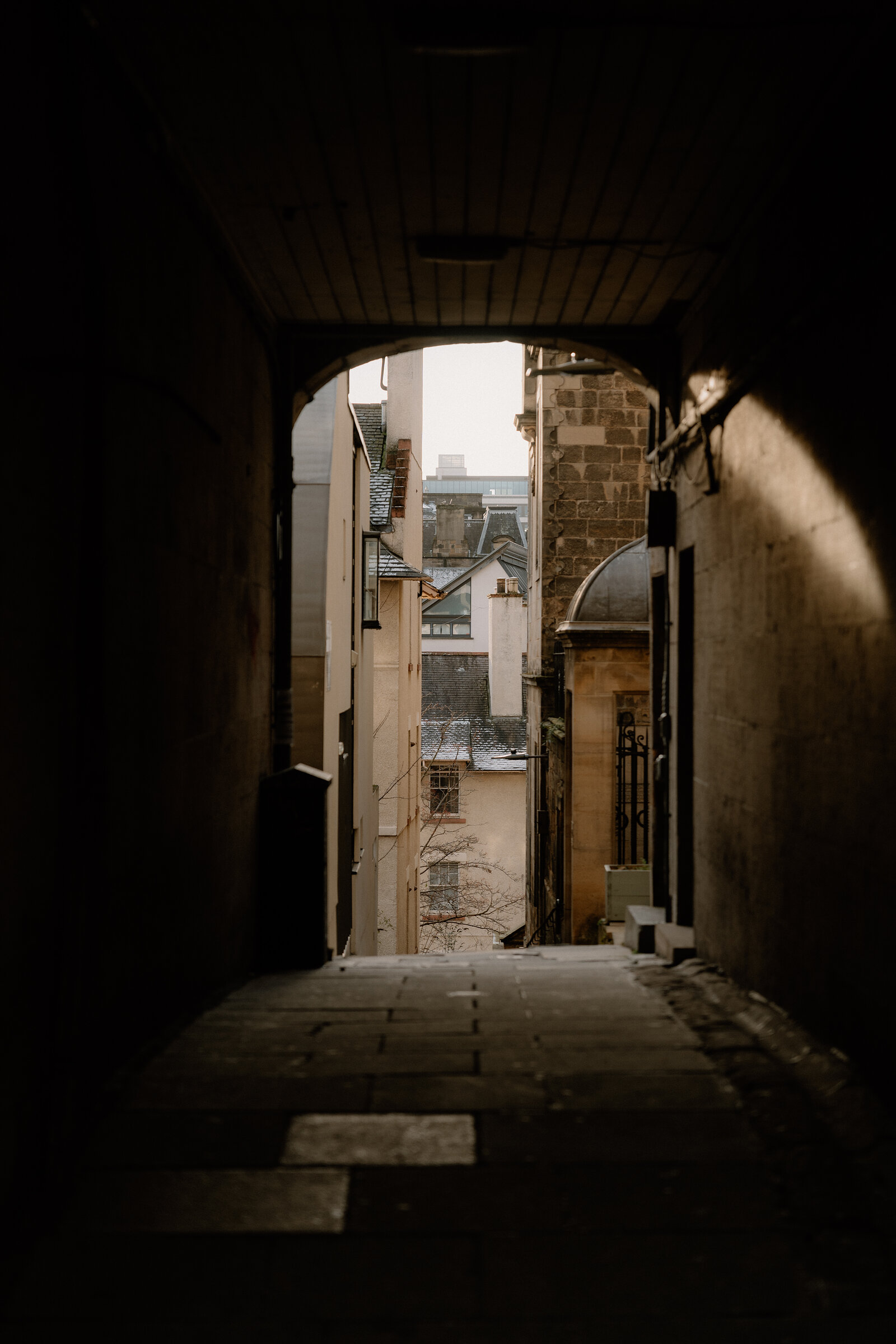 A stone archway frames a view of chimneys and rooftops down a narrow Edinburgh close.