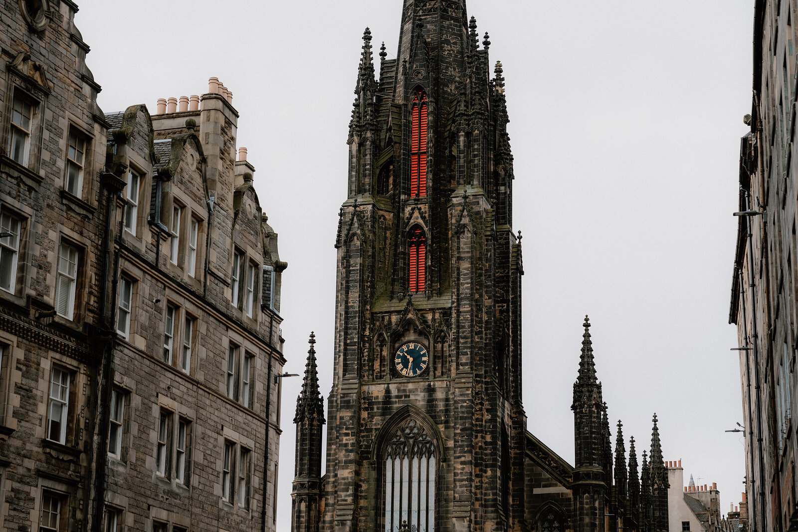 The Hub's spire rises above tenement rooftops on the Royal Mile, a red stained-glass window lit within.