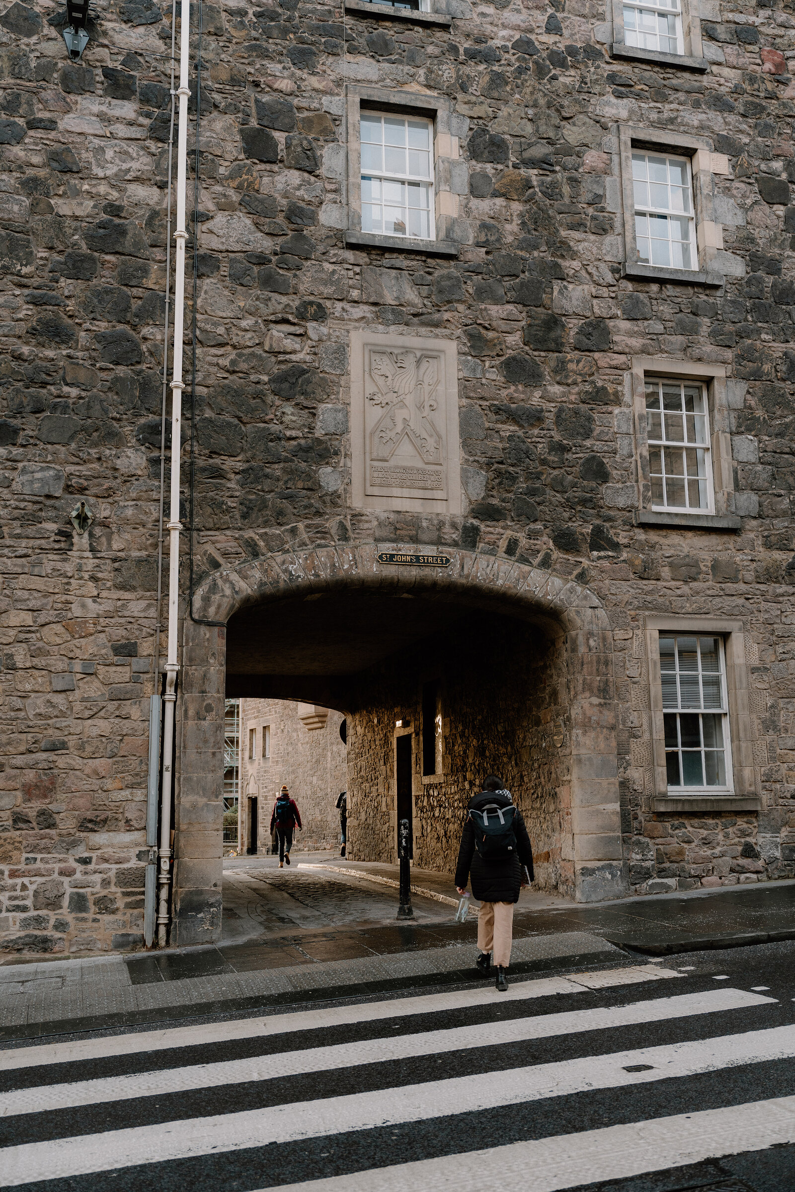 A pedestrian walks beneath a carved crest through a stone archway inscribed with a street name.