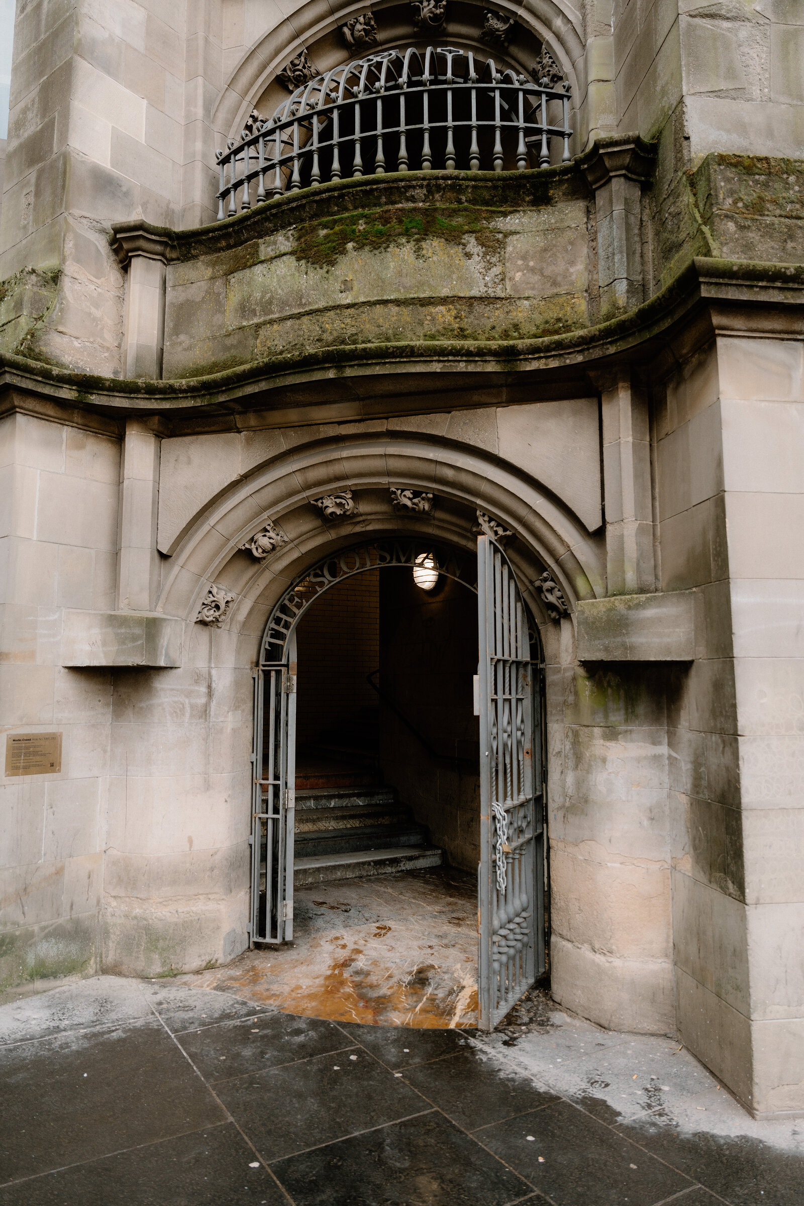 An arched stone gateway with wrought-iron gates opens onto a mossy staircase at a grand Edinburgh building.