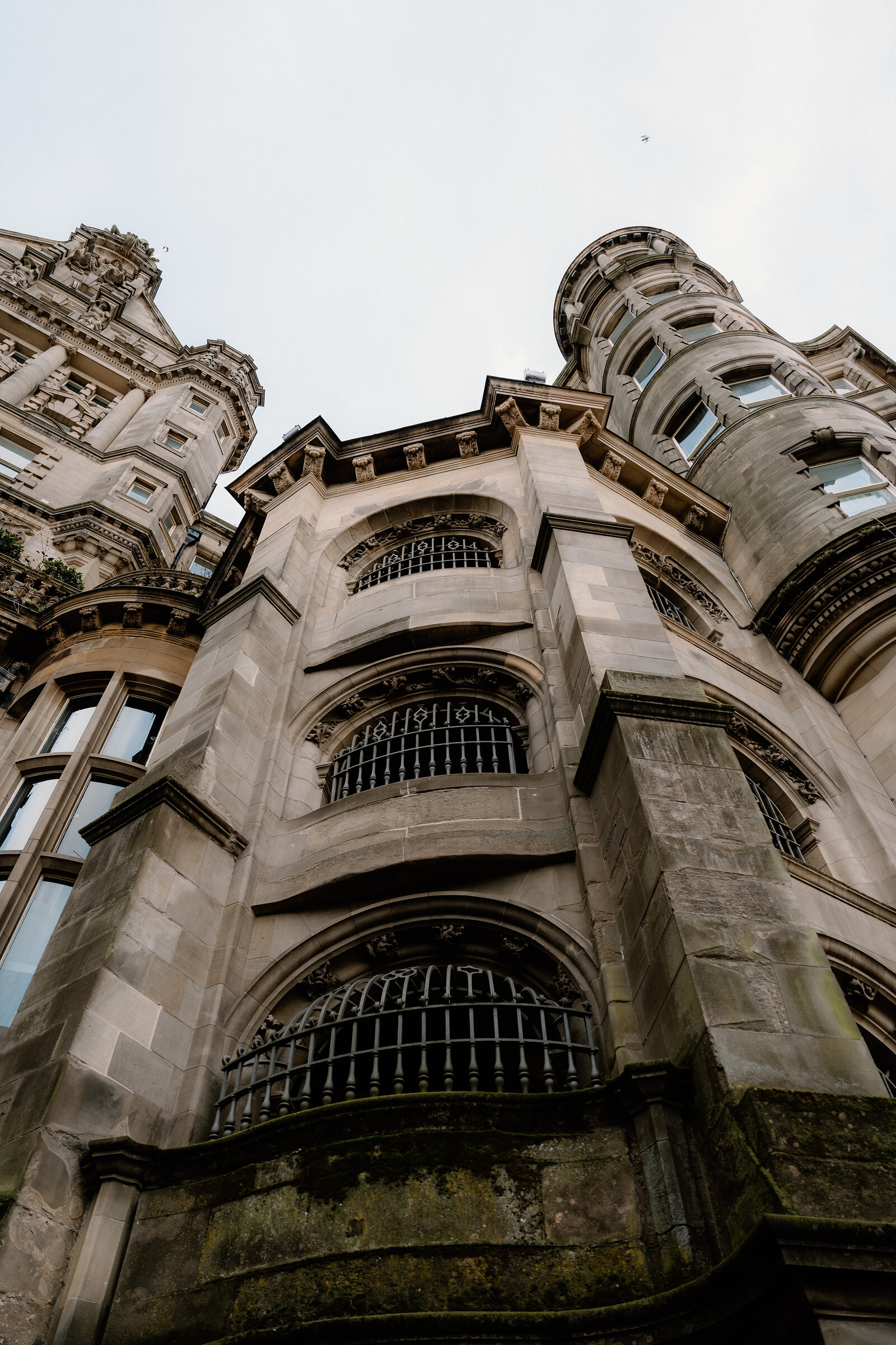 Turreted stone towers with arched windows rise above a grand Edinburgh building.