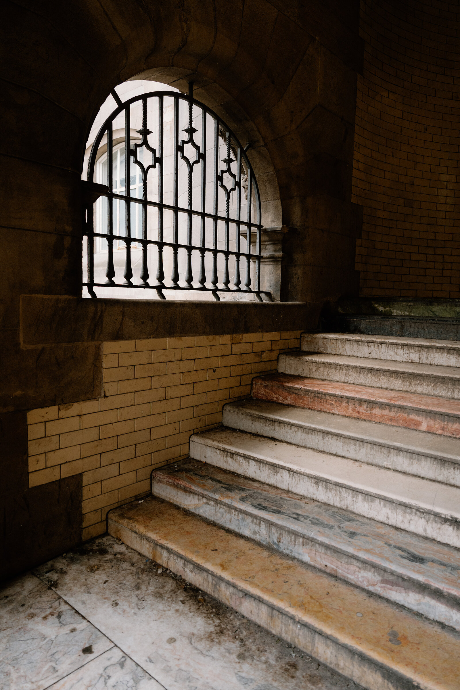Marble steps lead up to an arched, iron-latticed window in a stone archway.