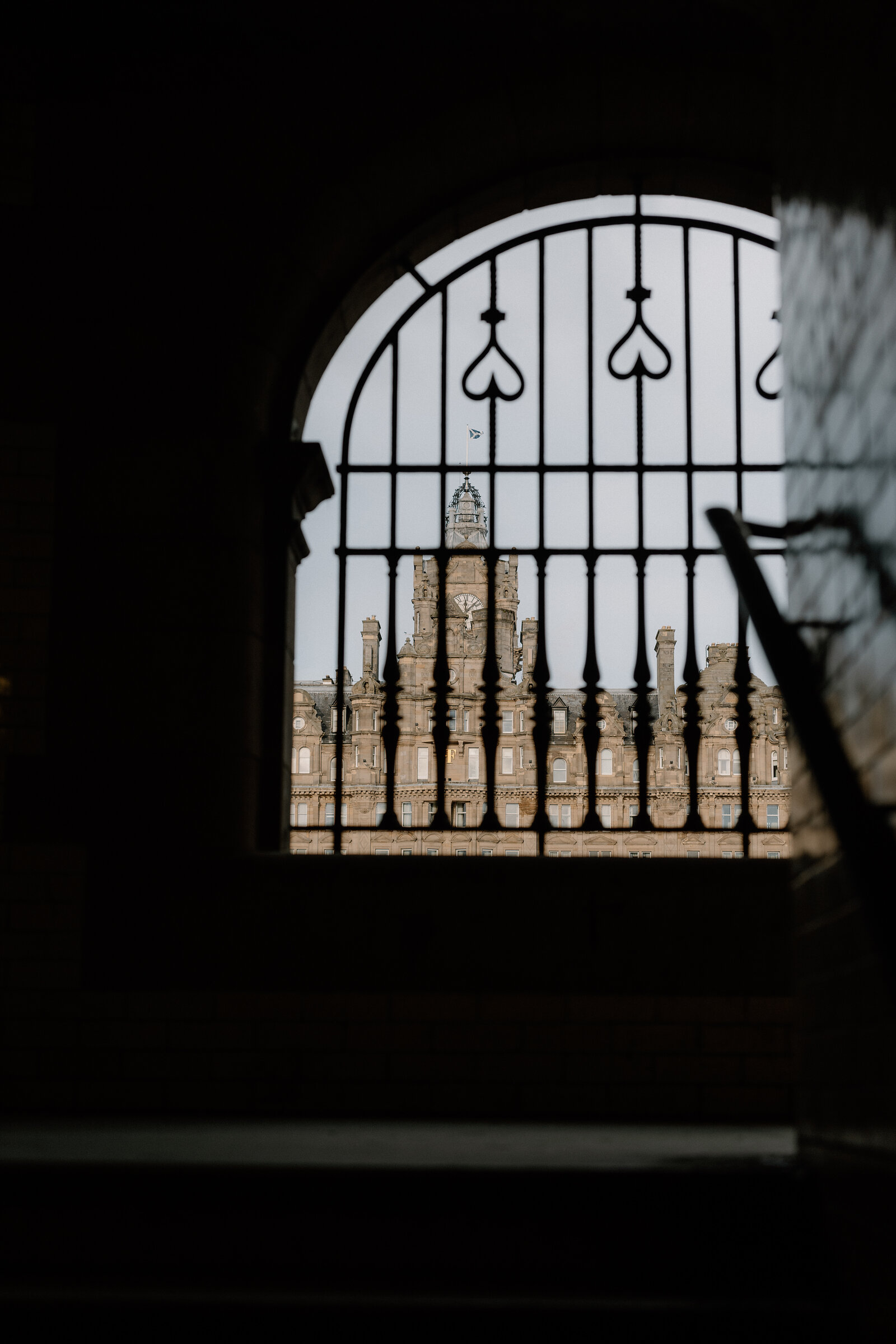 An ornate iron gate frames a distant clock tower against the sky.