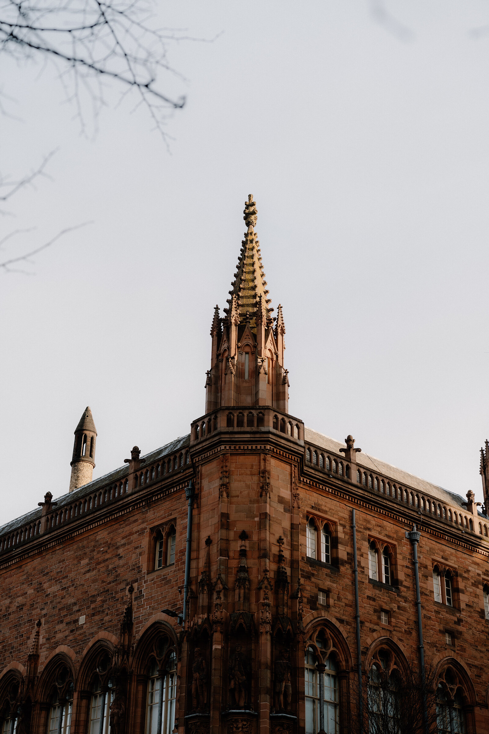 A carved stone spire crowns the corner of a red sandstone gothic building.