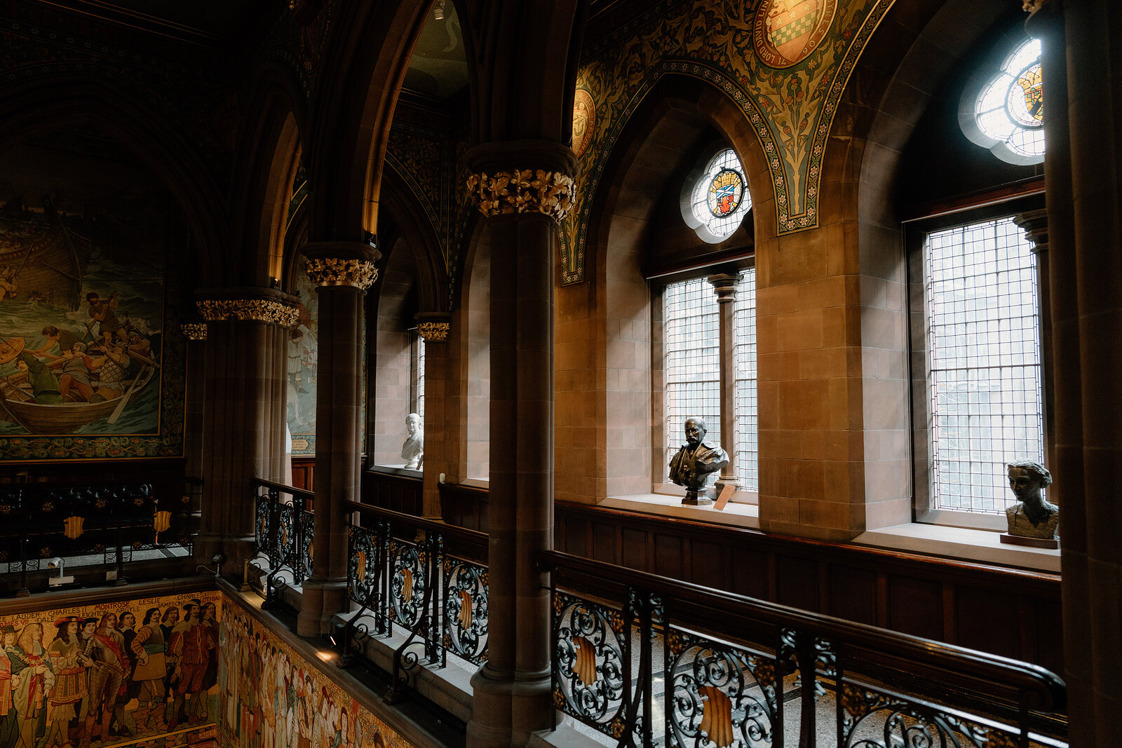 Stone columns and stained-glass windows overlook a wrought-iron gallery railing above a painted frieze.