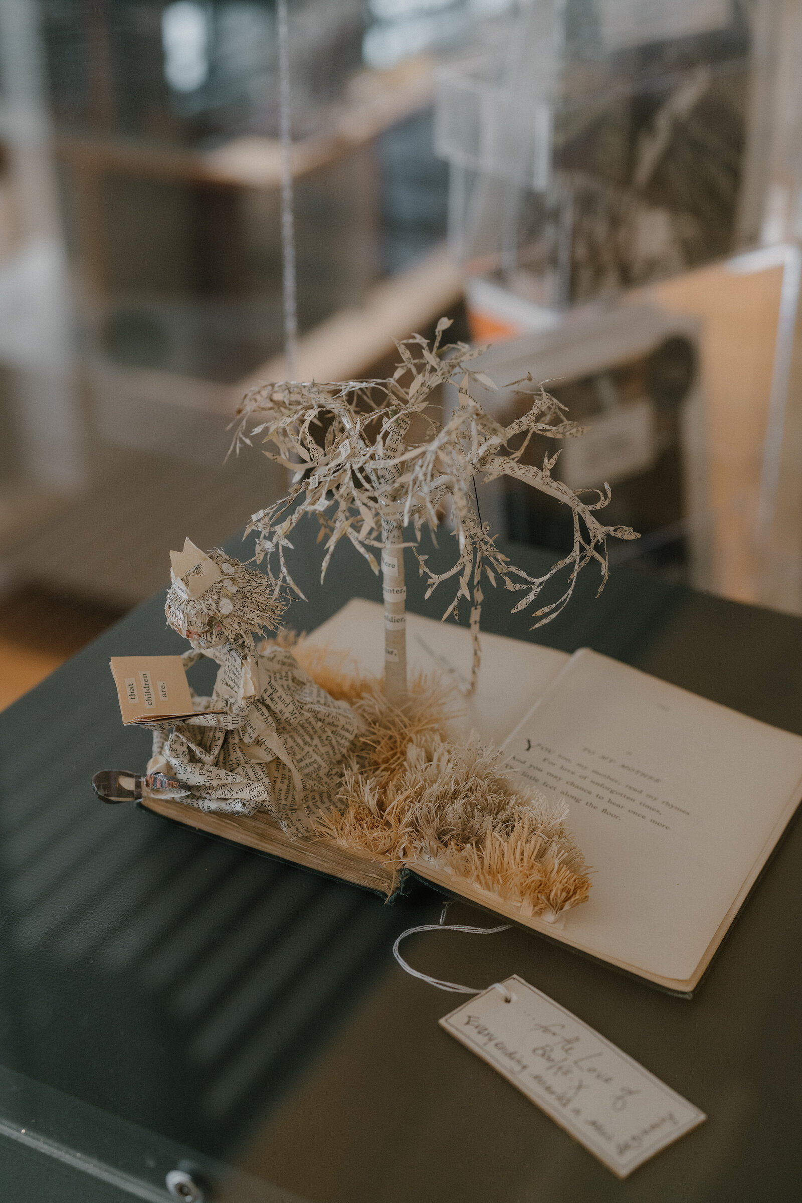 A paper sculpture of a girl beneath a frosted tree rises from an open storybook in a museum display case.