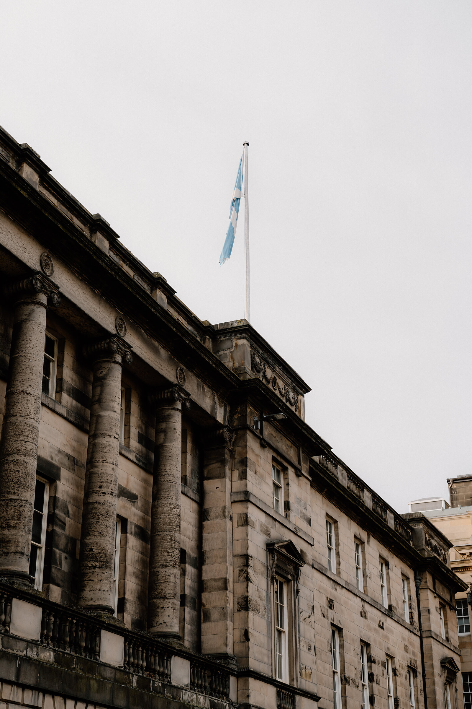A Saltire flag flies above a colonnaded stone building.