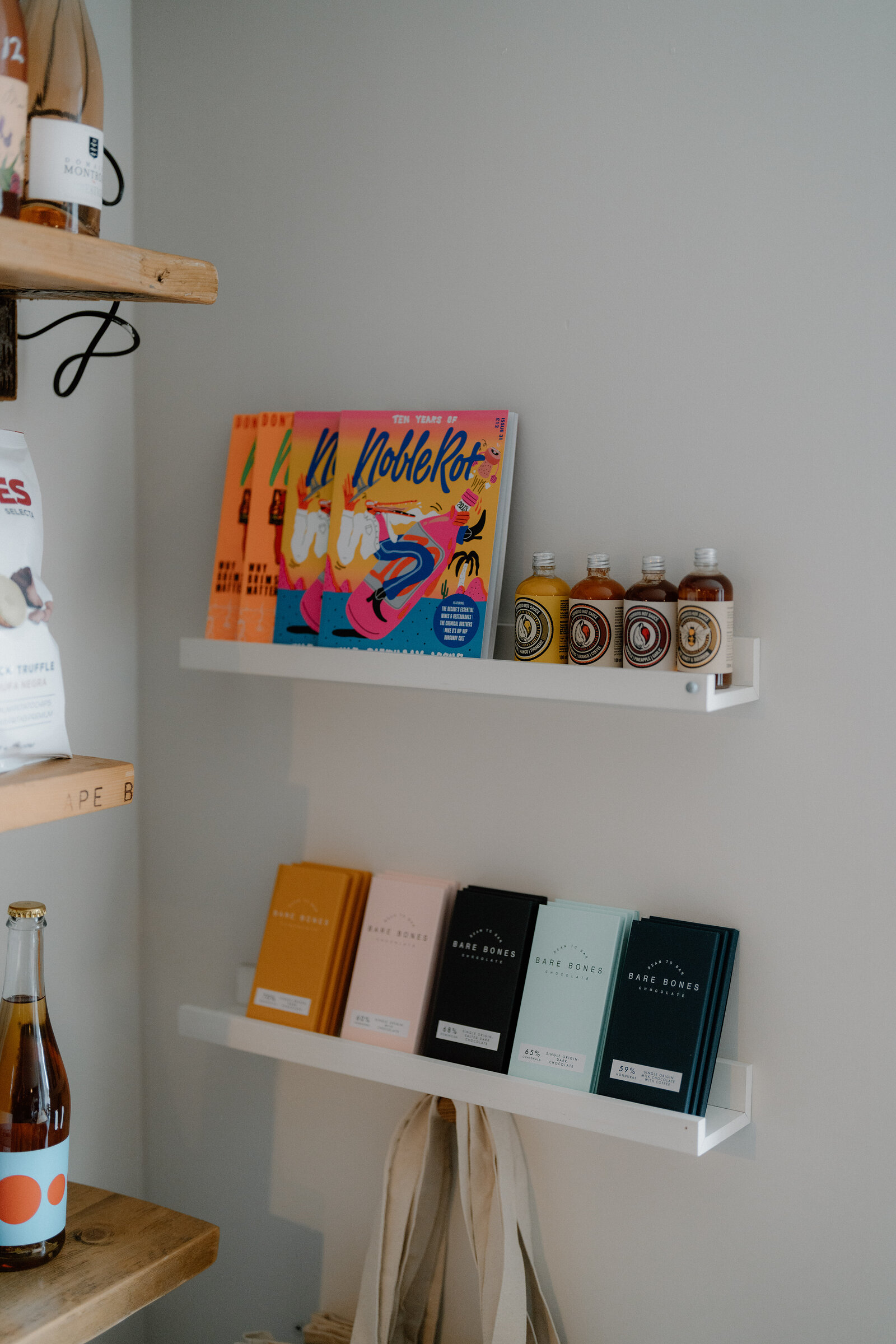 Bottled drinks and books sit on floating shelves in a wine shop, a wine bottle on the counter below.