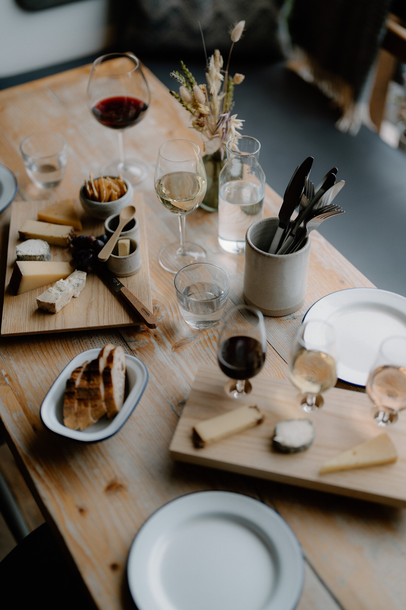 Cheese boards, sliced bread and glasses of wine cover a wooden table set for a tasting.