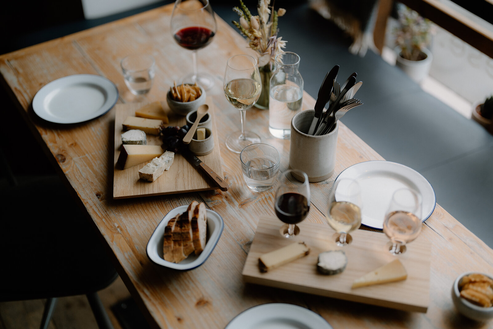 Cheese boards, glasses of wine and small plates cover a wooden table set for a tasting.