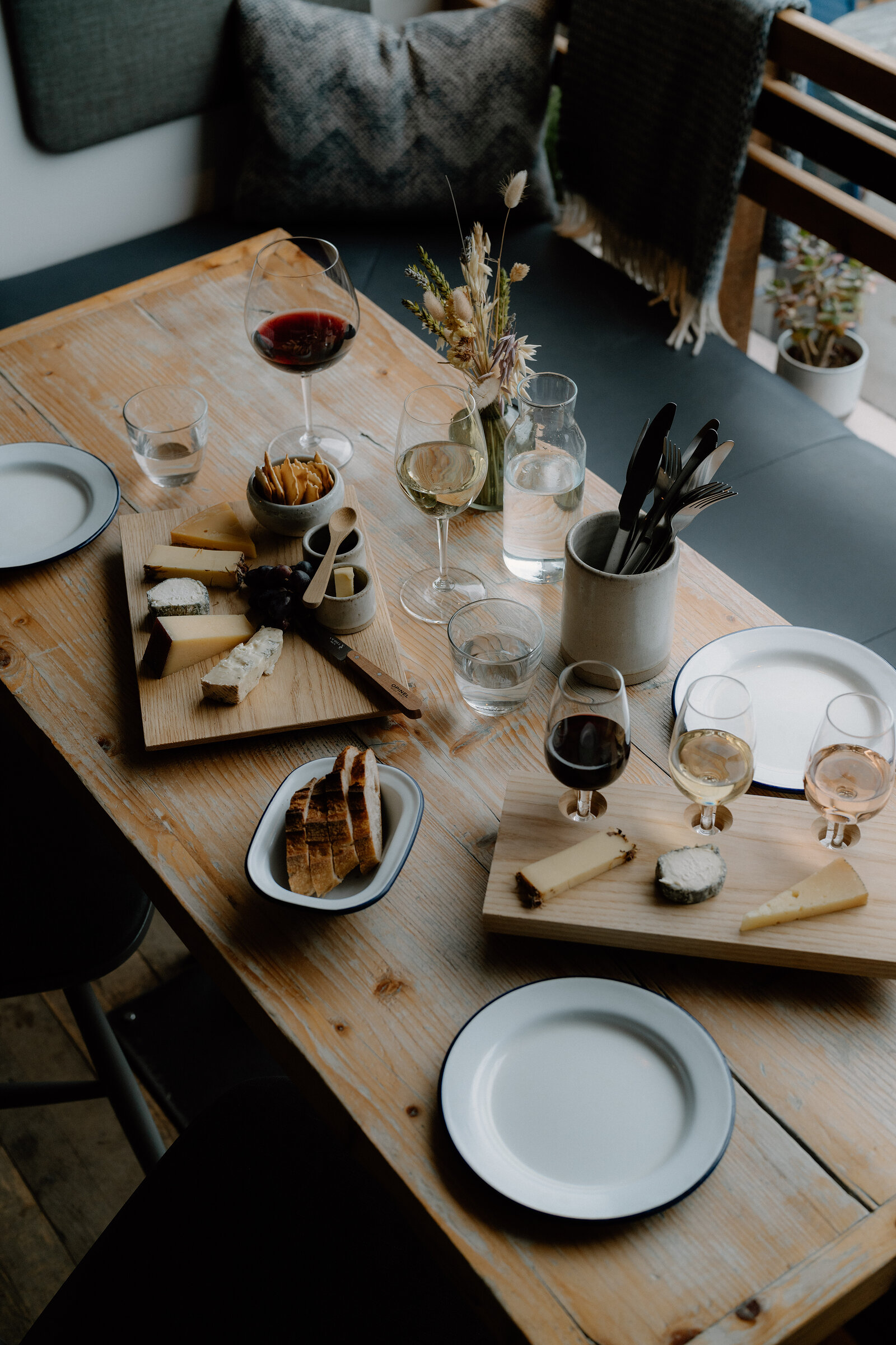 Wine glasses and cheese boards sit on a wooden table before a cushioned banquette.