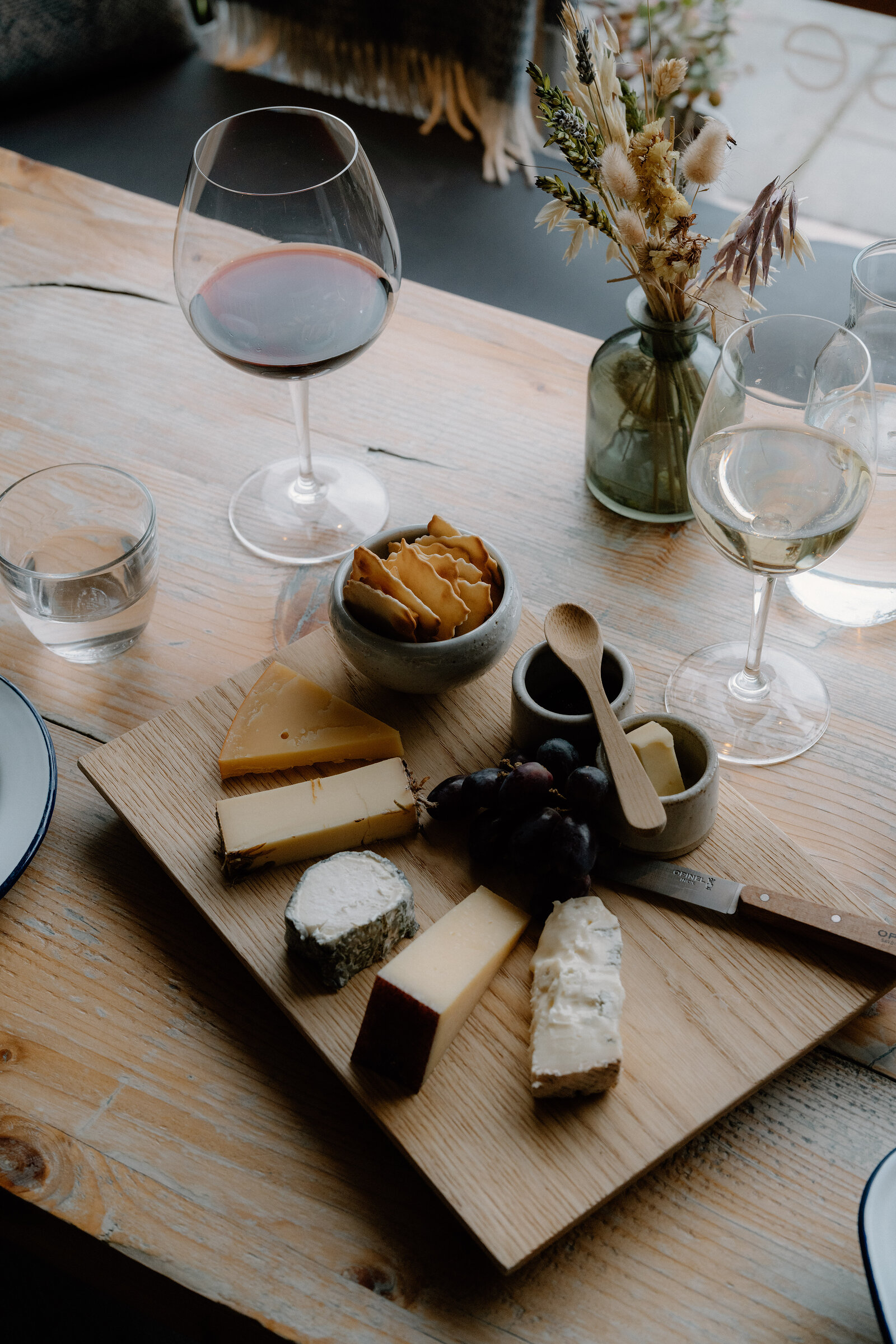 A cheese board with grapes and crackers sits beside glasses of red and white wine.