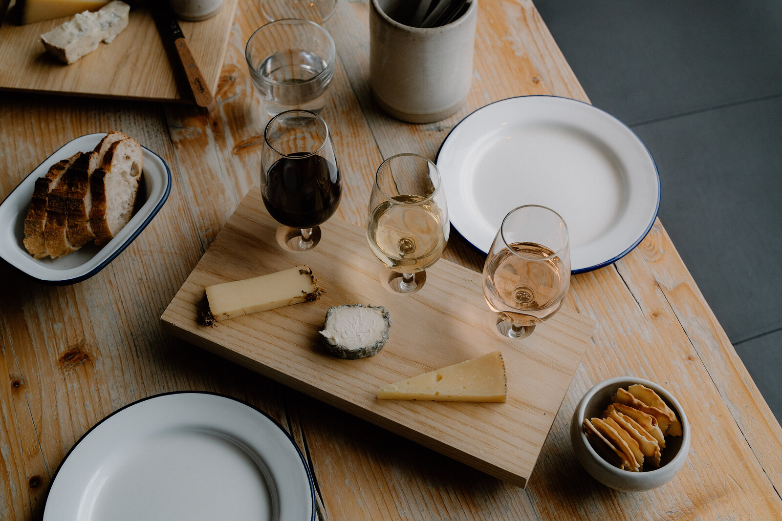 A cheese board and bowl of crackers sit beside glasses of red, white and rosé wine.