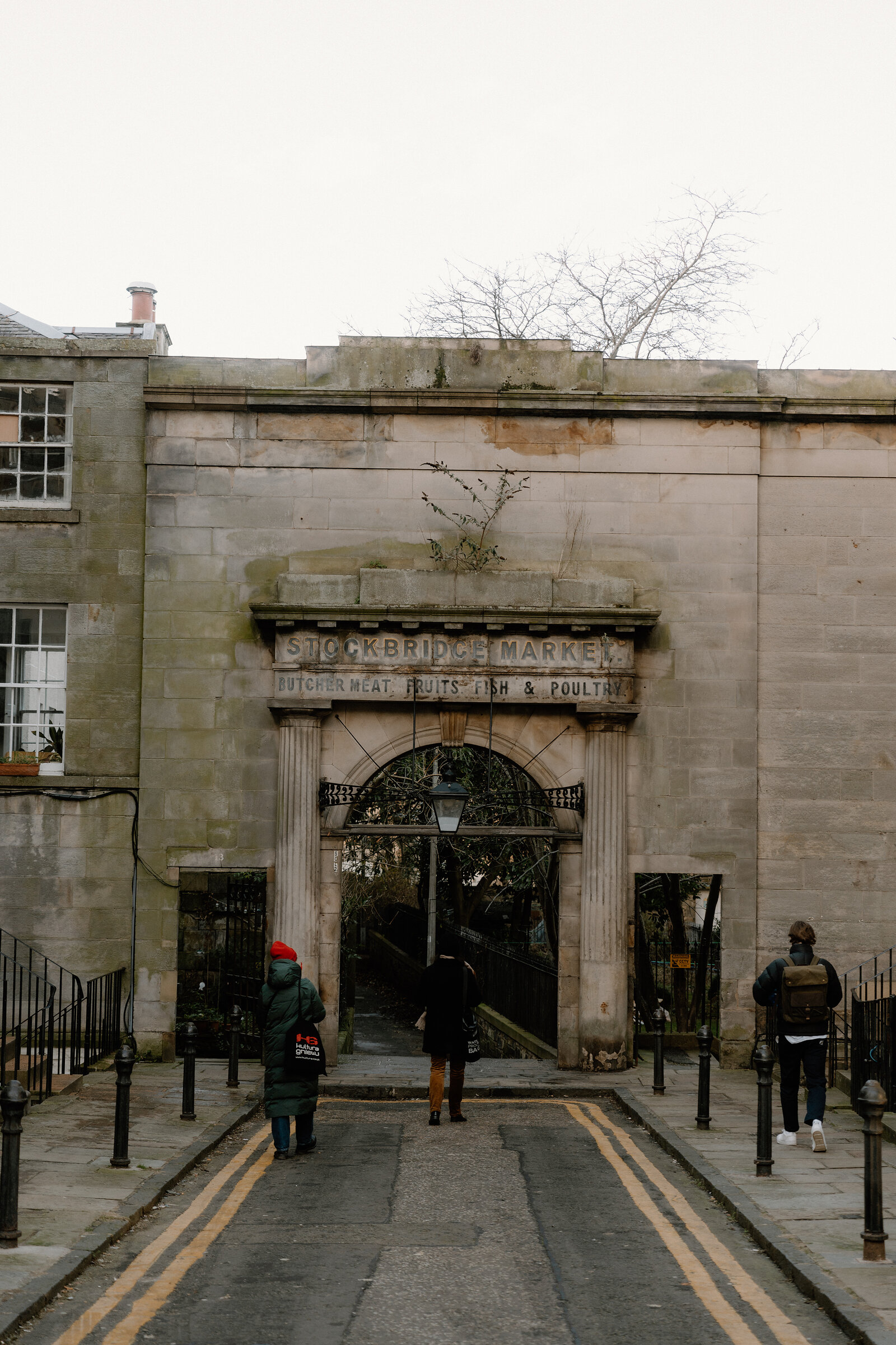 Pedestrians pass beneath a carved stone archway reading 'Stockbridge Market'.