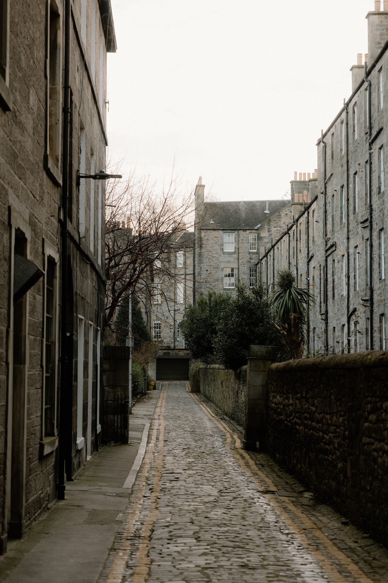 A cobbled lane runs between stone tenements toward a distant building.