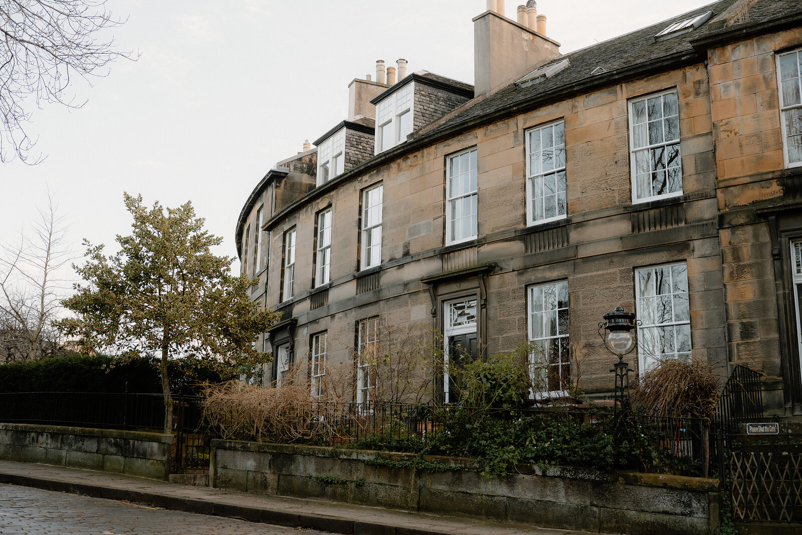 A curved row of sandstone tenements lines a quiet Edinburgh street.