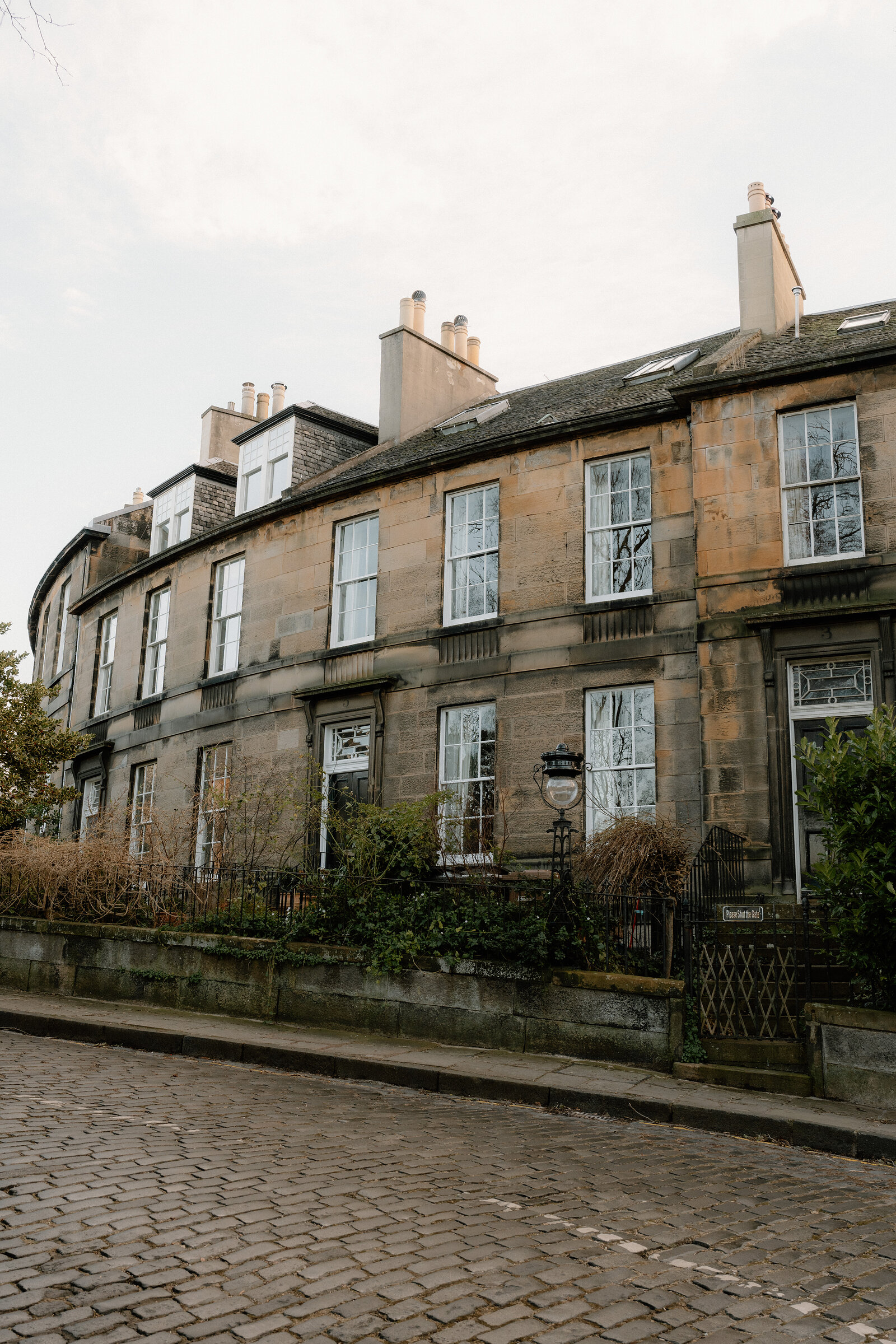 A curved sandstone tenement rises above a cobbled corner in Edinburgh.