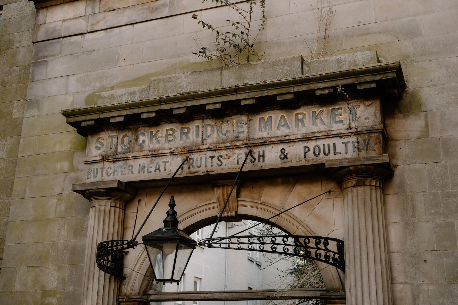 A carved stone sign reading 'Stockbridge Market, Butcher Meat, Fruits, Fish & Poultry' sits above an arched gateway.