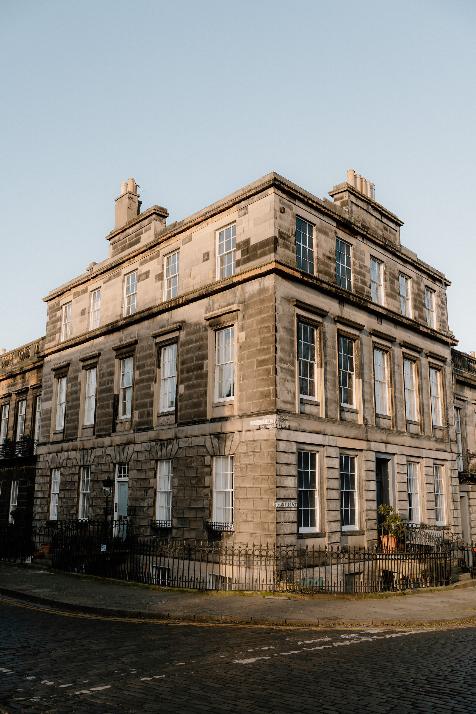 A corner sandstone tenement rises above a cobbled Edinburgh street at golden hour.