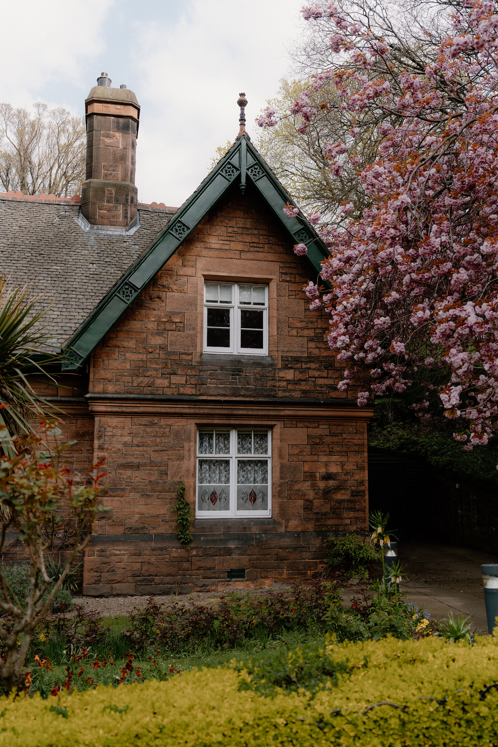A red sandstone gable with green-trimmed eaves rises beside a blossoming tree.