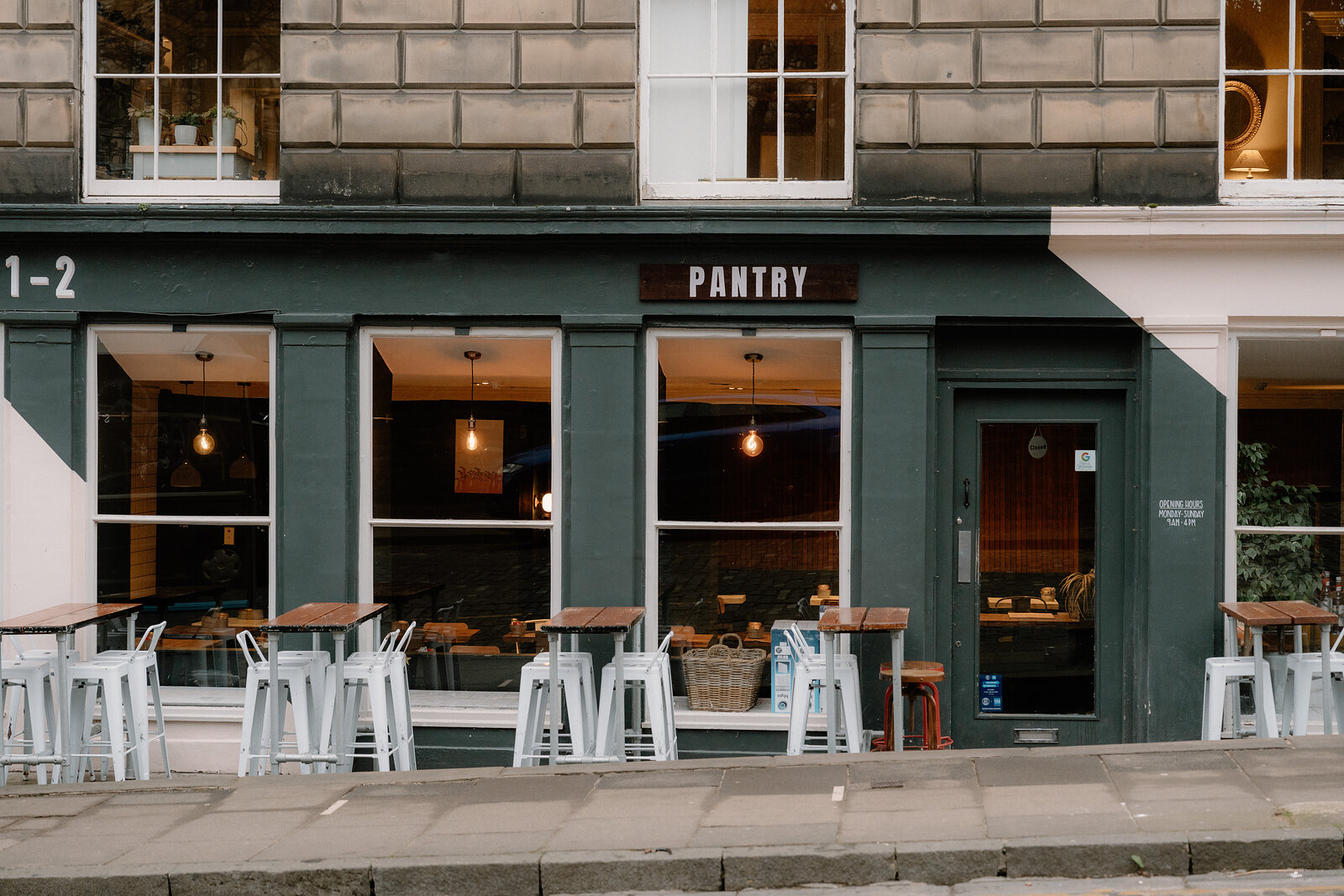 A sign reading 'Pantry' marks a green-painted shopfront with outdoor stools and tables.