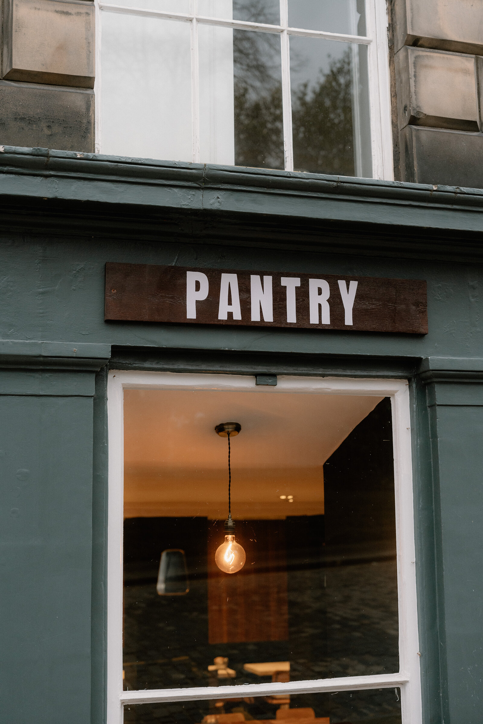 A wooden sign reading 'Pantry' hangs above a lit doorway with a bare bulb pendant.